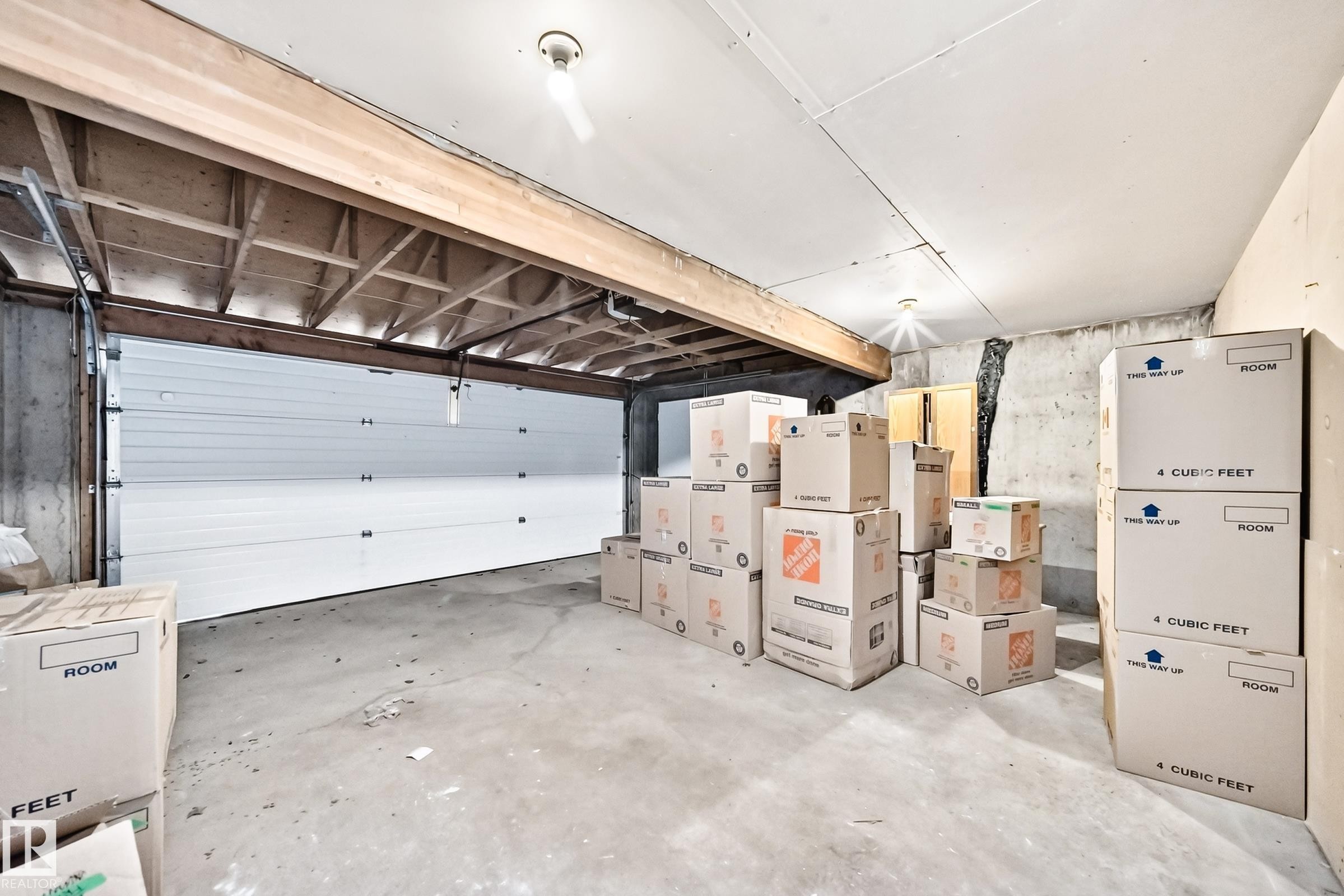 Concrete floor garage with a white sectional door, exposed ceiling joists, and a bare bulb light fixture - 4208 Ramsay Road Nw, Edmonton, AB - Indoor Photo Showing Garage