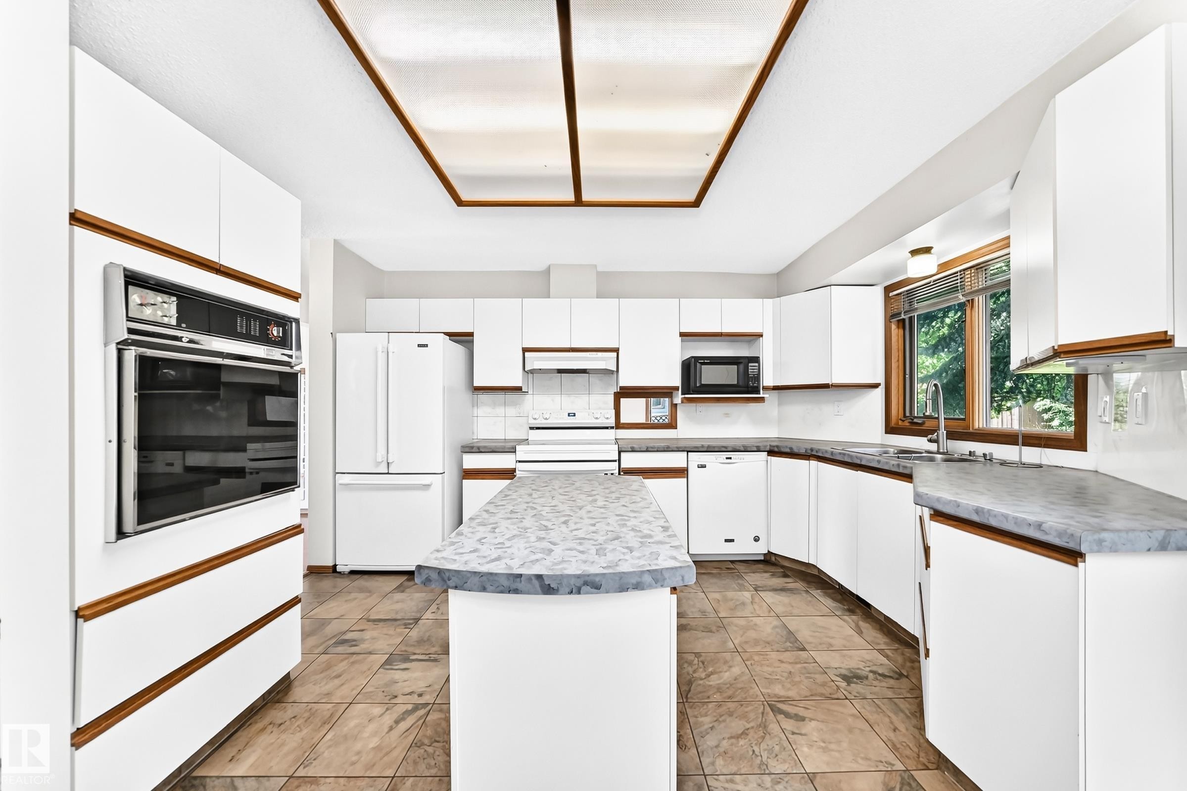 Kitchen featuring white cabinetry with wood-tone accents, a built-in wall oven, a center island with a gray countertop, and tile flooring - 4208 Ramsay Road Nw, Edmonton, AB - Indoor Photo Showing Kitchen