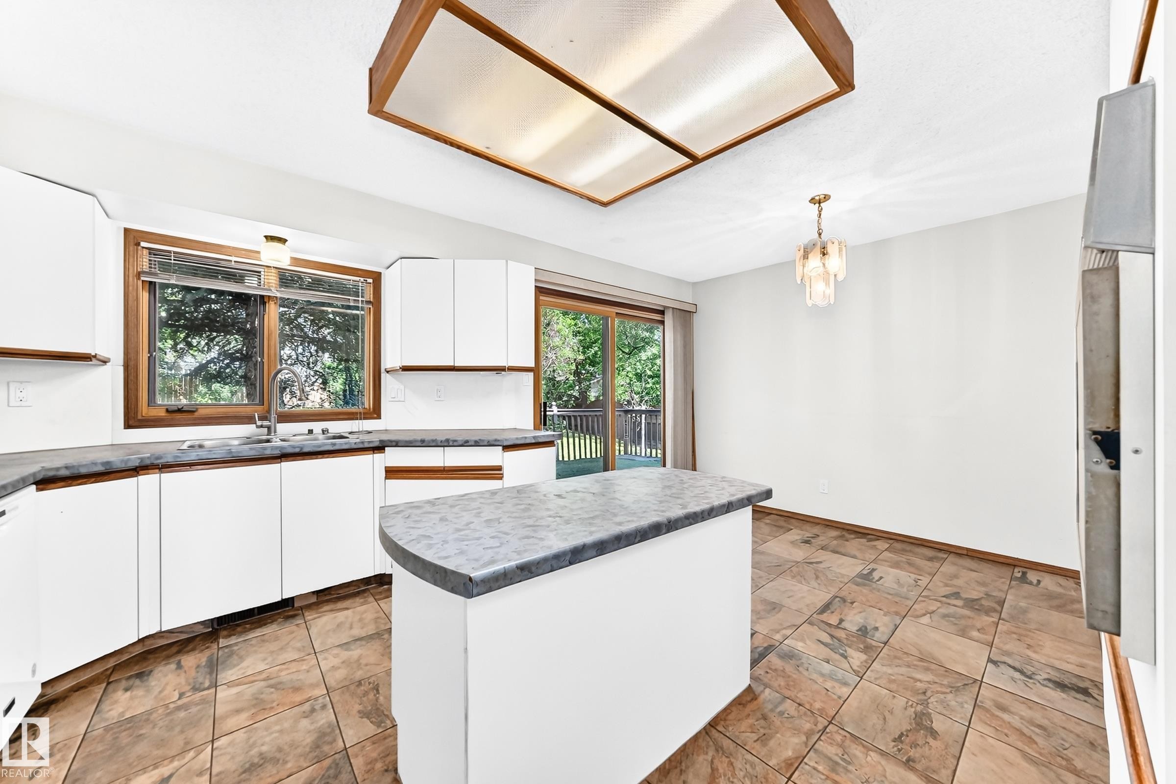 Kitchen featuring white cabinetry, a single basin sink with a gooseneck faucet, a peninsula with countertop seating, and tile flooring - 4208 Ramsay Road Nw, Edmonton, AB - Indoor Photo Showing Kitchen With Double Sink