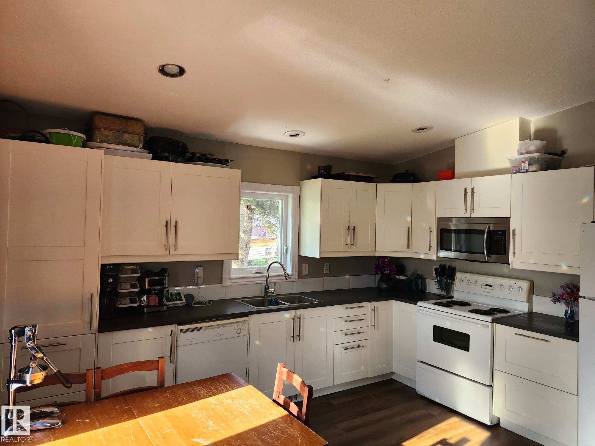 Modern kitchen featuring white cabinetry, dark countertops, an undermount sink, and recessed lighting - 5273 50 Street, Mayerthorpe, AB - Indoor Photo Showing Kitchen With Double Sink