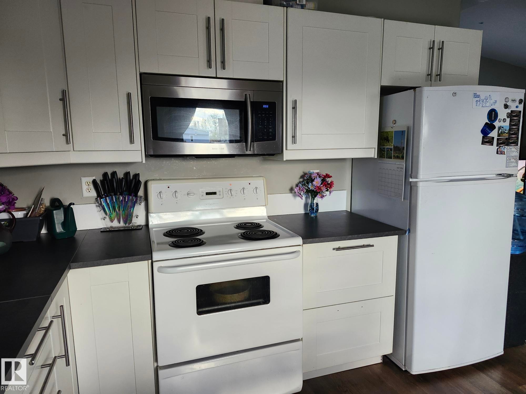 White cabinetry with brushed nickel hardware, dark countertops, and a white electric range with a stainless steel microwave - 5273 50 Street, Mayerthorpe, AB - Indoor Photo Showing Kitchen