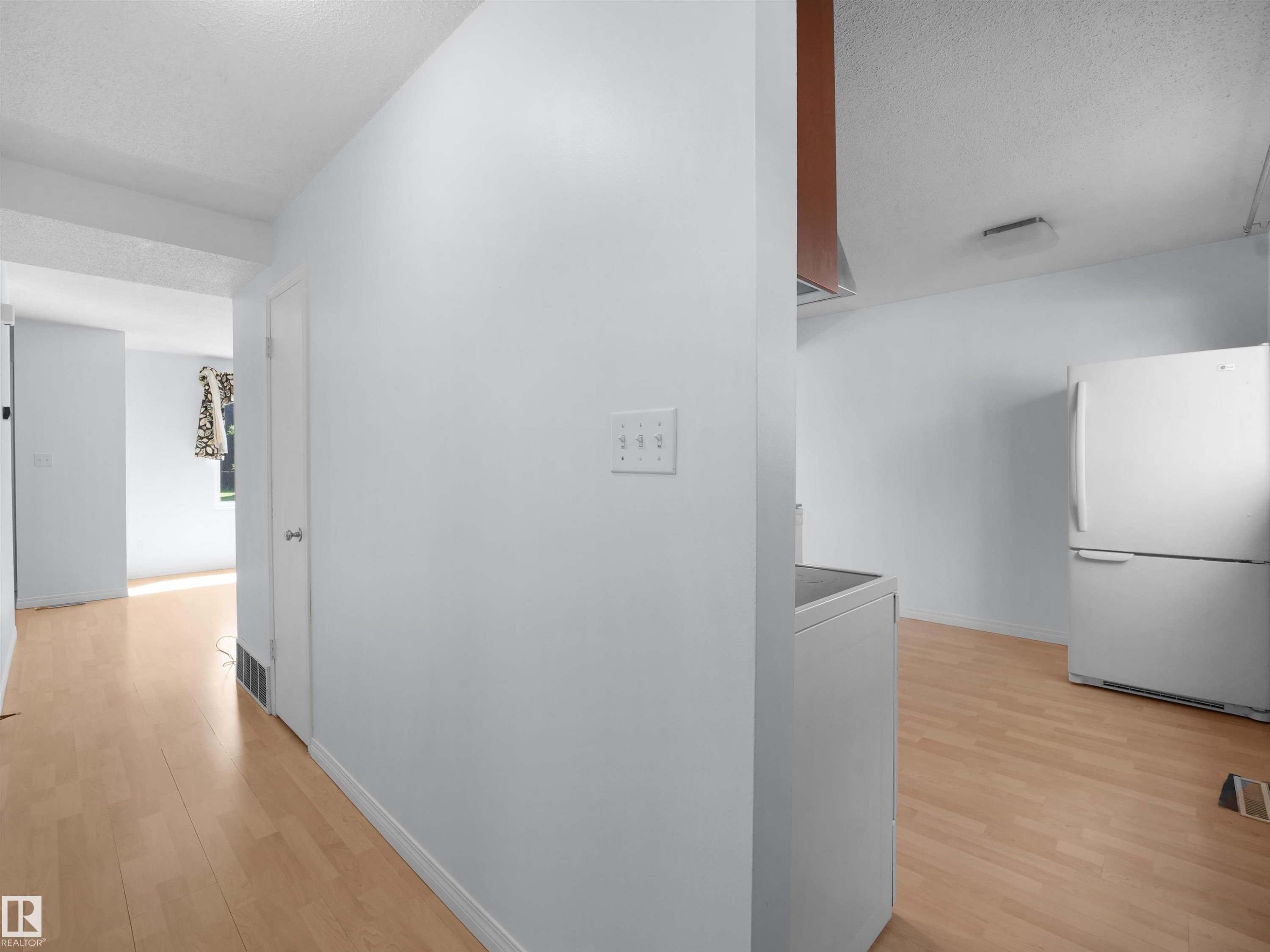Light wood-finish flooring extending into multiple spaces, white walls, and a white refrigerator - 10446 55 Avenue Nw, Edmonton, AB - Indoor