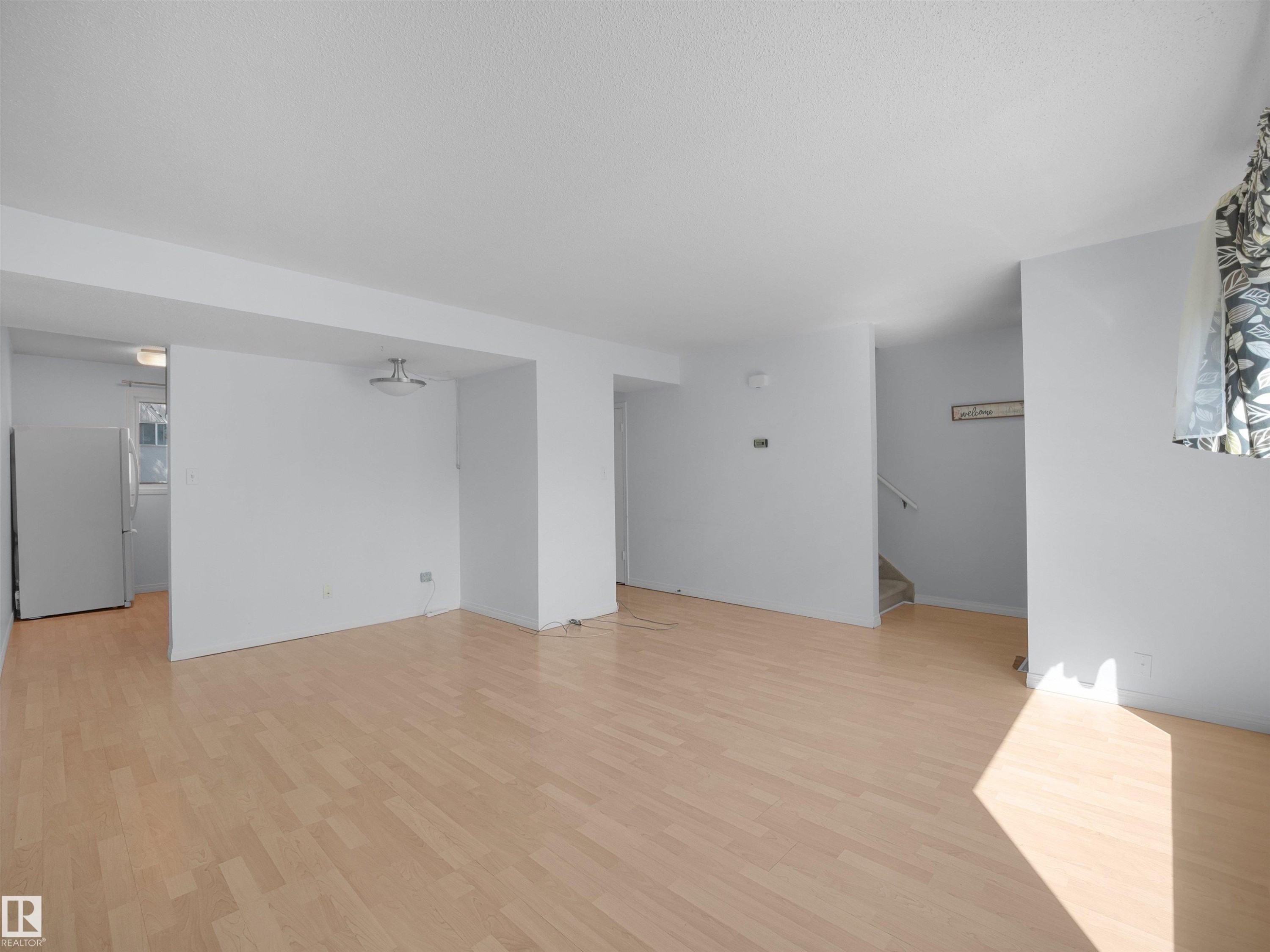 Spacious interior featuring light wood-finish flooring, white painted walls, and a semi-flush mount ceiling fixture - 10446 55 Avenue Nw, Edmonton, AB - Indoor Photo Showing Other Room