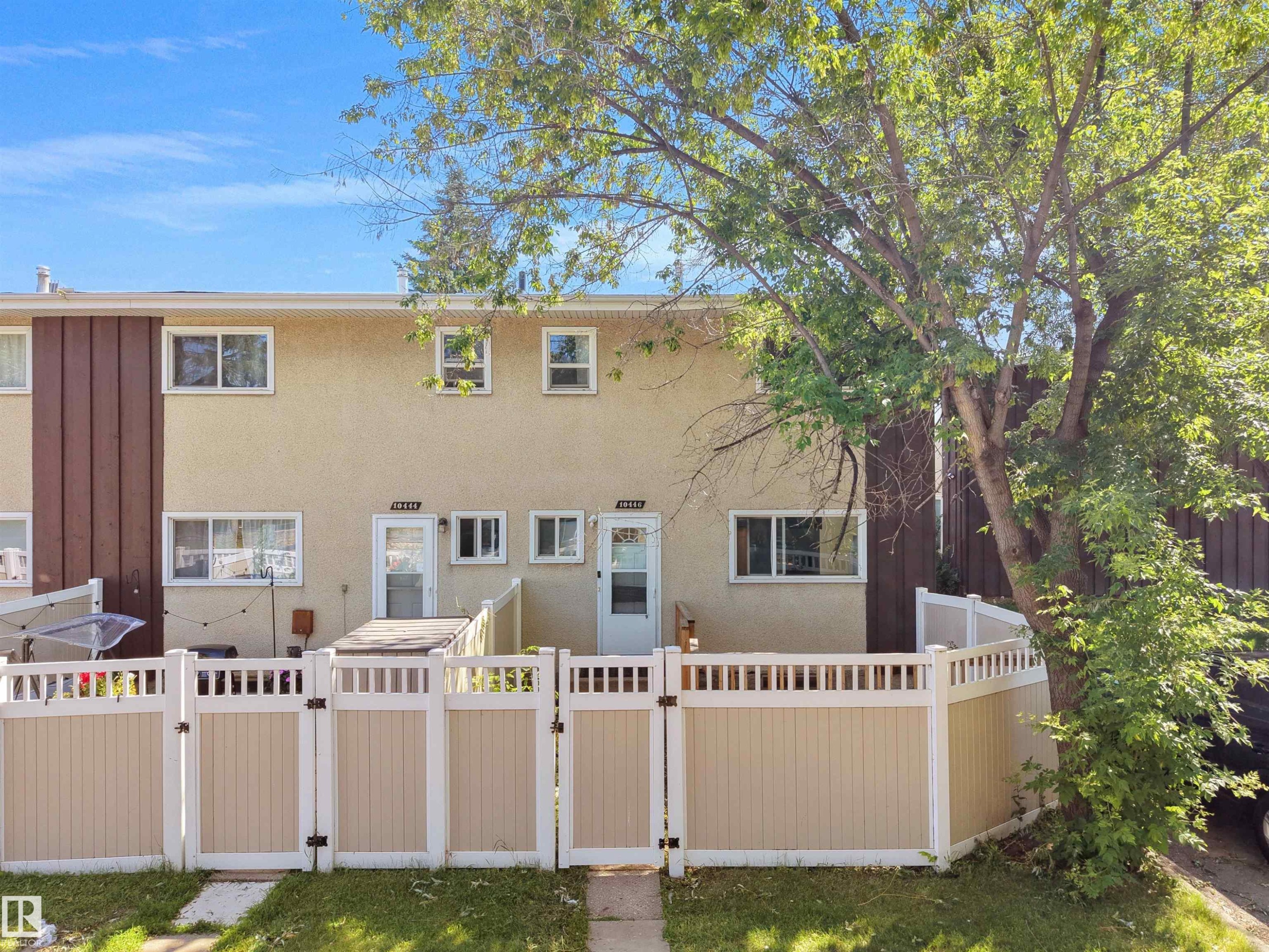 Exterior of a two-story townhouse featuring a tan stucco facade and white-trimmed windows - 10446 55 Avenue Nw, Edmonton, AB -