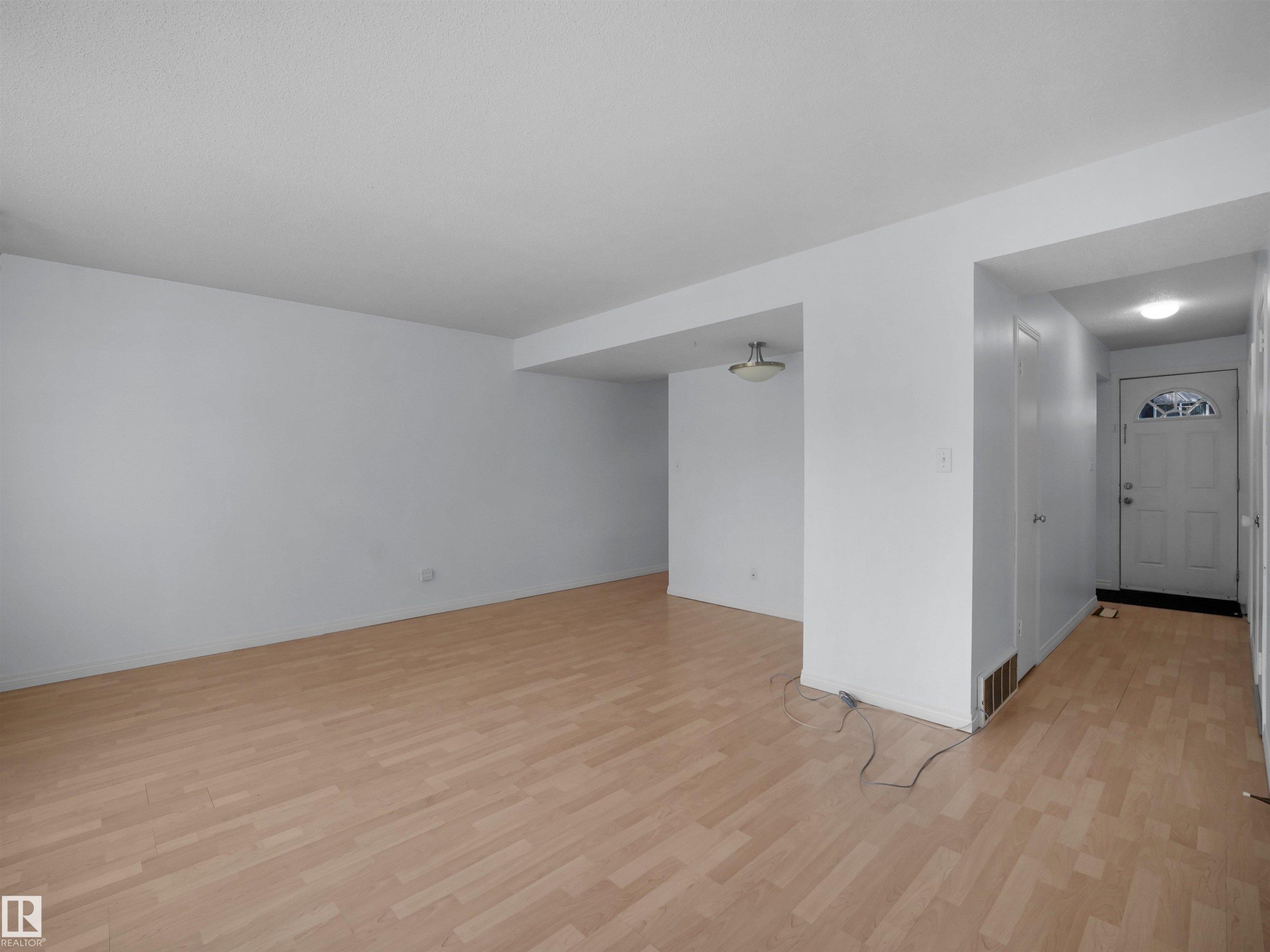 Open concept living area featuring light wood-finish flooring, white walls, and an overhead flush-mount light fixture - 10446 55 Avenue Nw, Edmonton, AB - Indoor Photo Showing Other Room