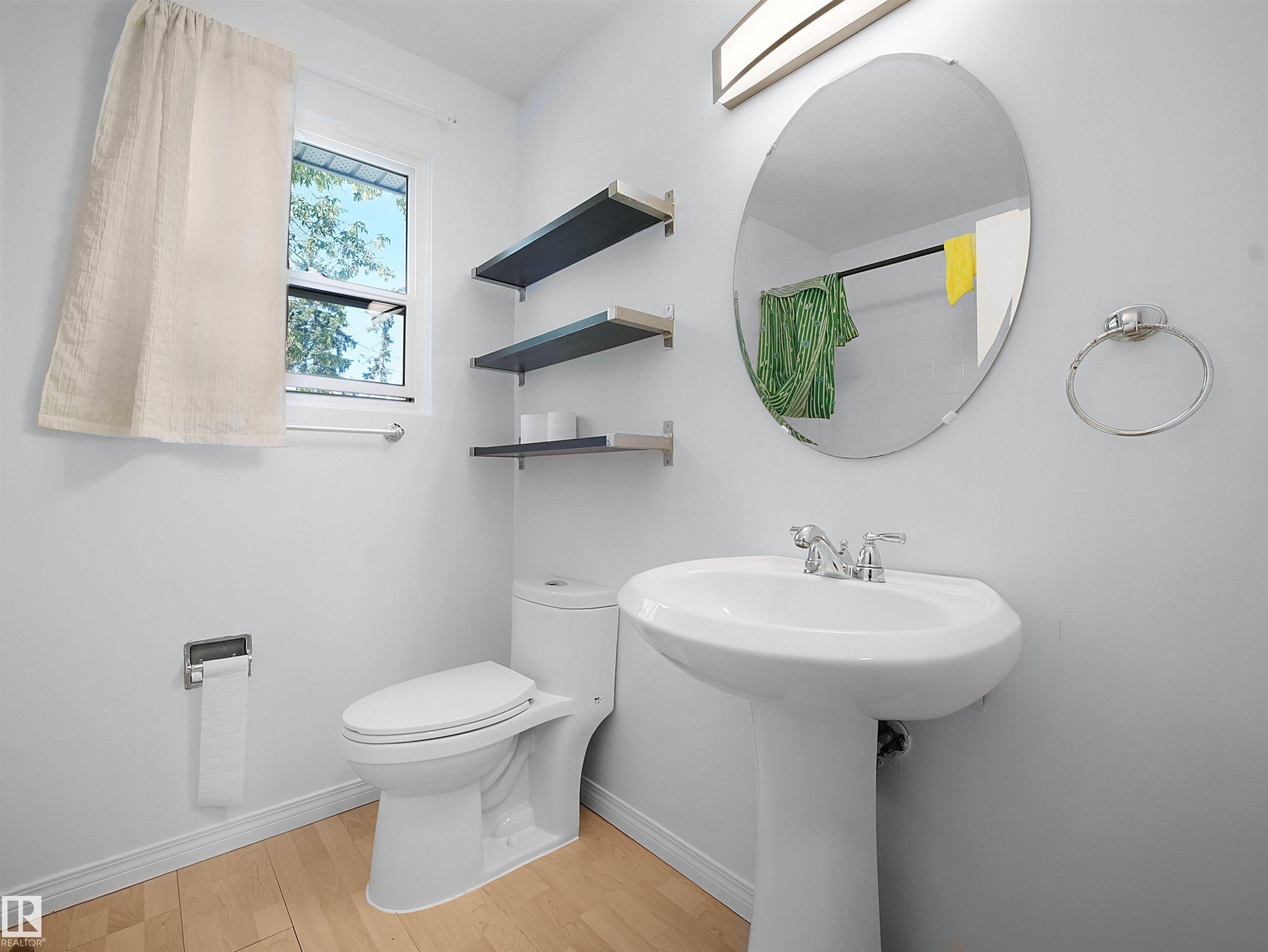 Pedestal sink with chrome faucet, oval mirror, and wall-mounted light fixture - 10446 55 Avenue Nw, Edmonton, AB - Indoor Photo Showing Bathroom