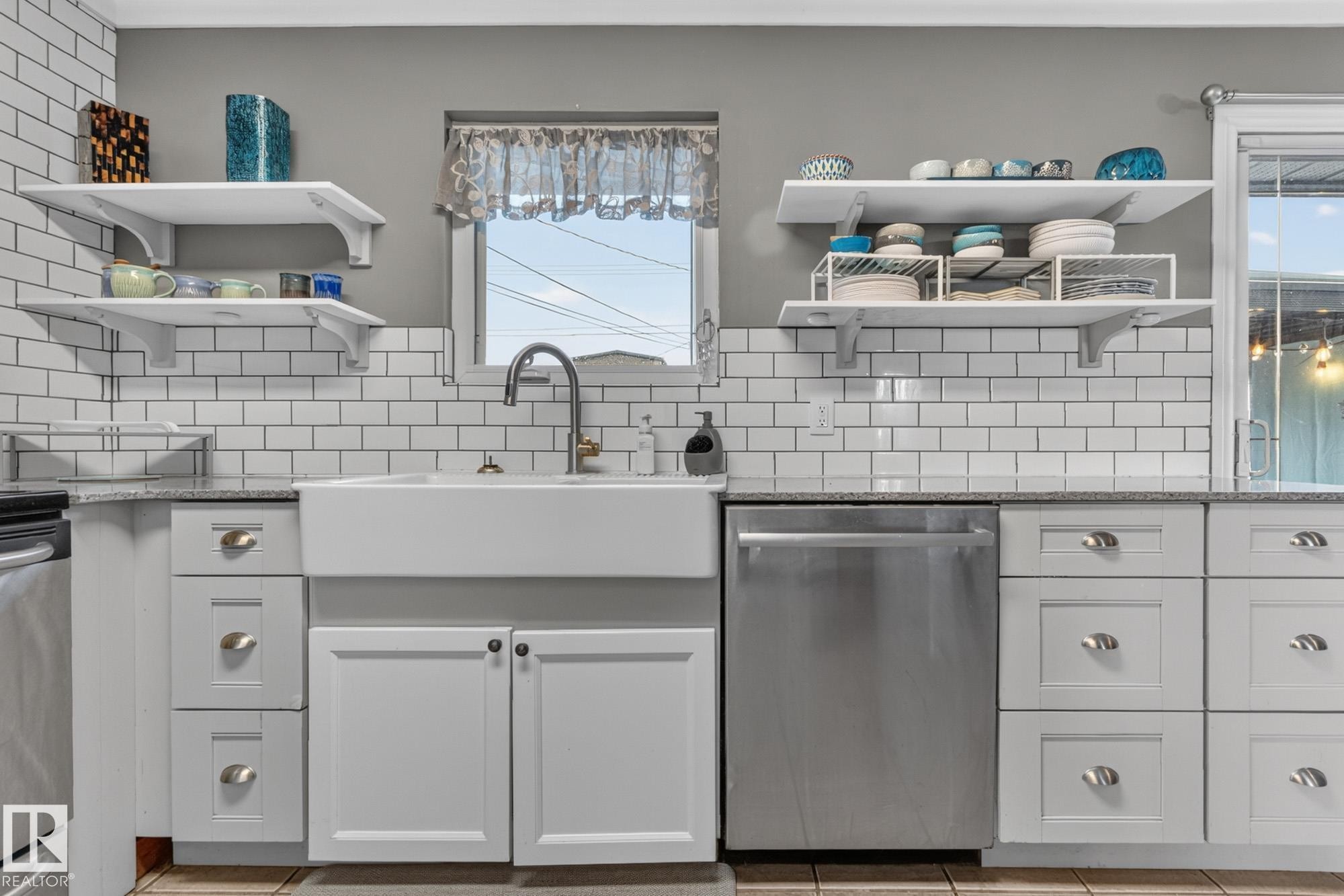 Kitchen featuring a white farmhouse sink with a gooseneck faucet, light gray cabinetry with varied drawer and door configurations, white subway tile backsplash, and granite-style countertops - 5307 104 Avenue Nw, Edmonton, AB - Indoor Photo Showing Kitchen With Upgraded Kitchen