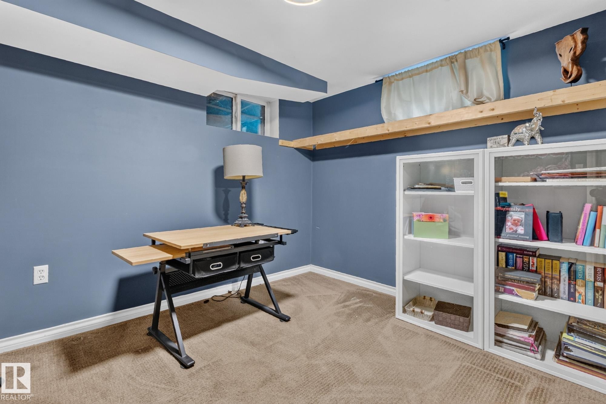 Carpeted room featuring a window, built-in shelving, a full wall shelf, and blue wall paint - 5307 104 Avenue Nw, Edmonton, AB - Indoor Photo Showing Other Room