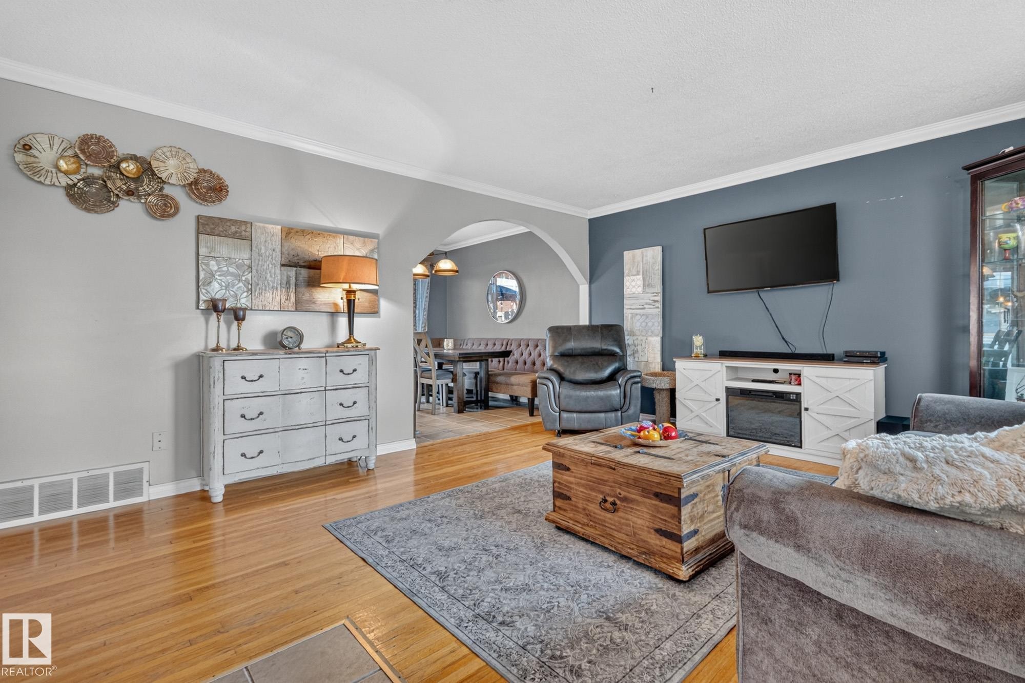 Spacious living area featuring hardwood flooring, crown molding, a built-in media console with an electric fireplace, an arched entryway, and recessed lighting in the dining area - 5307 104 Avenue Nw, Edmonton, AB - Indoor Photo Showing Living Room
