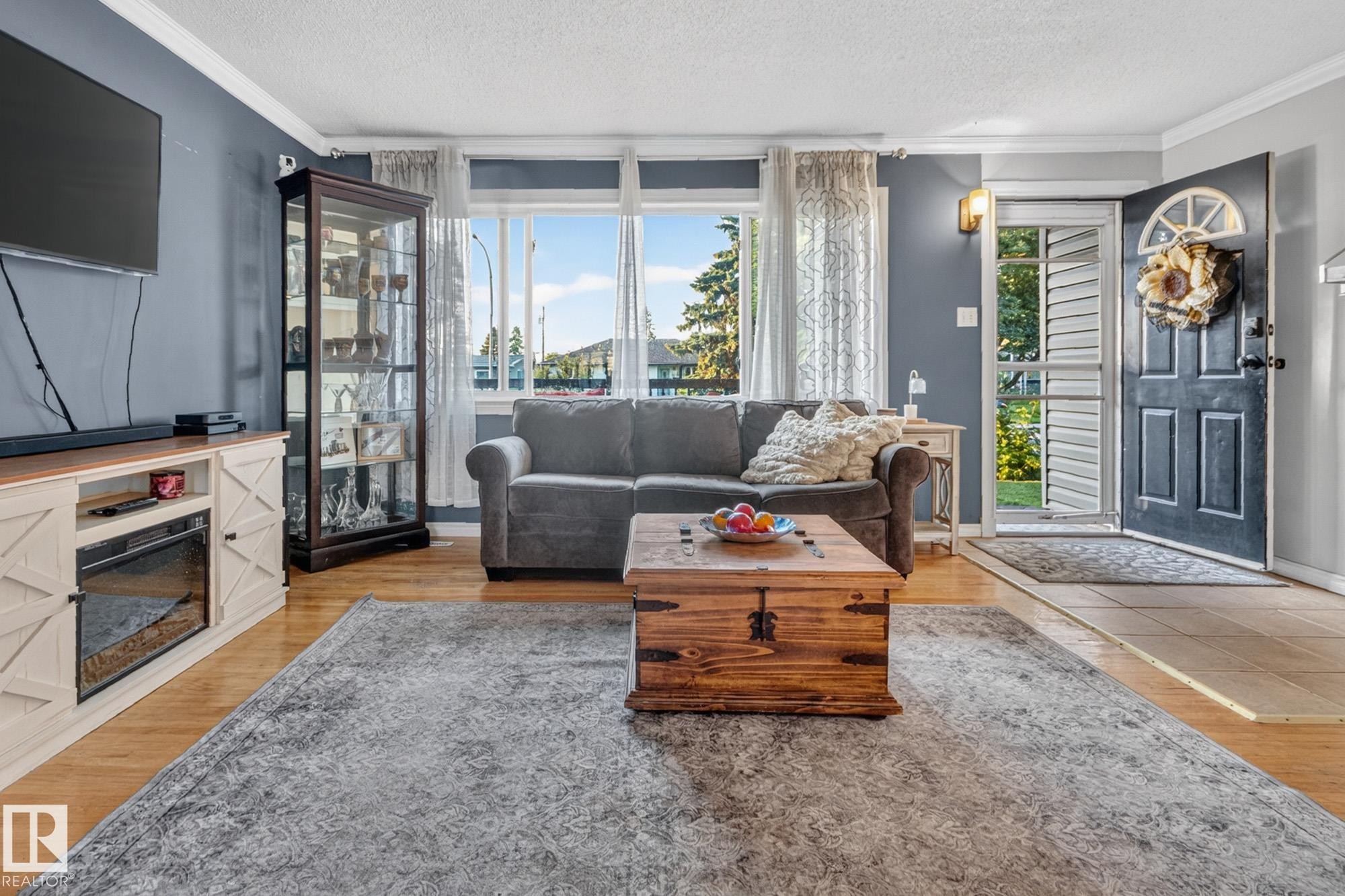 Living room with hardwood-finish flooring, a broad front window, and a built-in media console with an electric fireplace insert - 5307 104 Avenue Nw, Edmonton, AB - Indoor Photo Showing Living Room With Fireplace