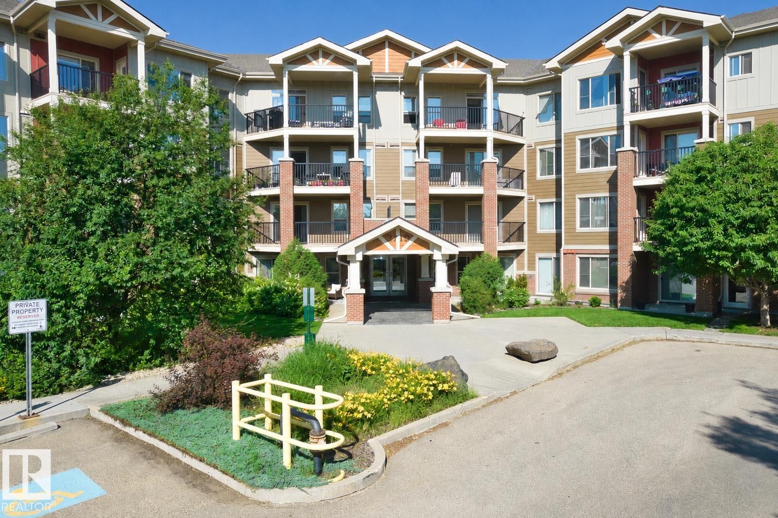 Multi-story residential building featuring balconies with black railings, brick column accents, and a central covered entrance with a gabled roofline - #317 3719 Whitelaw Ln Nw, Edmonton, AB - Outdoor With Balcony With Facade