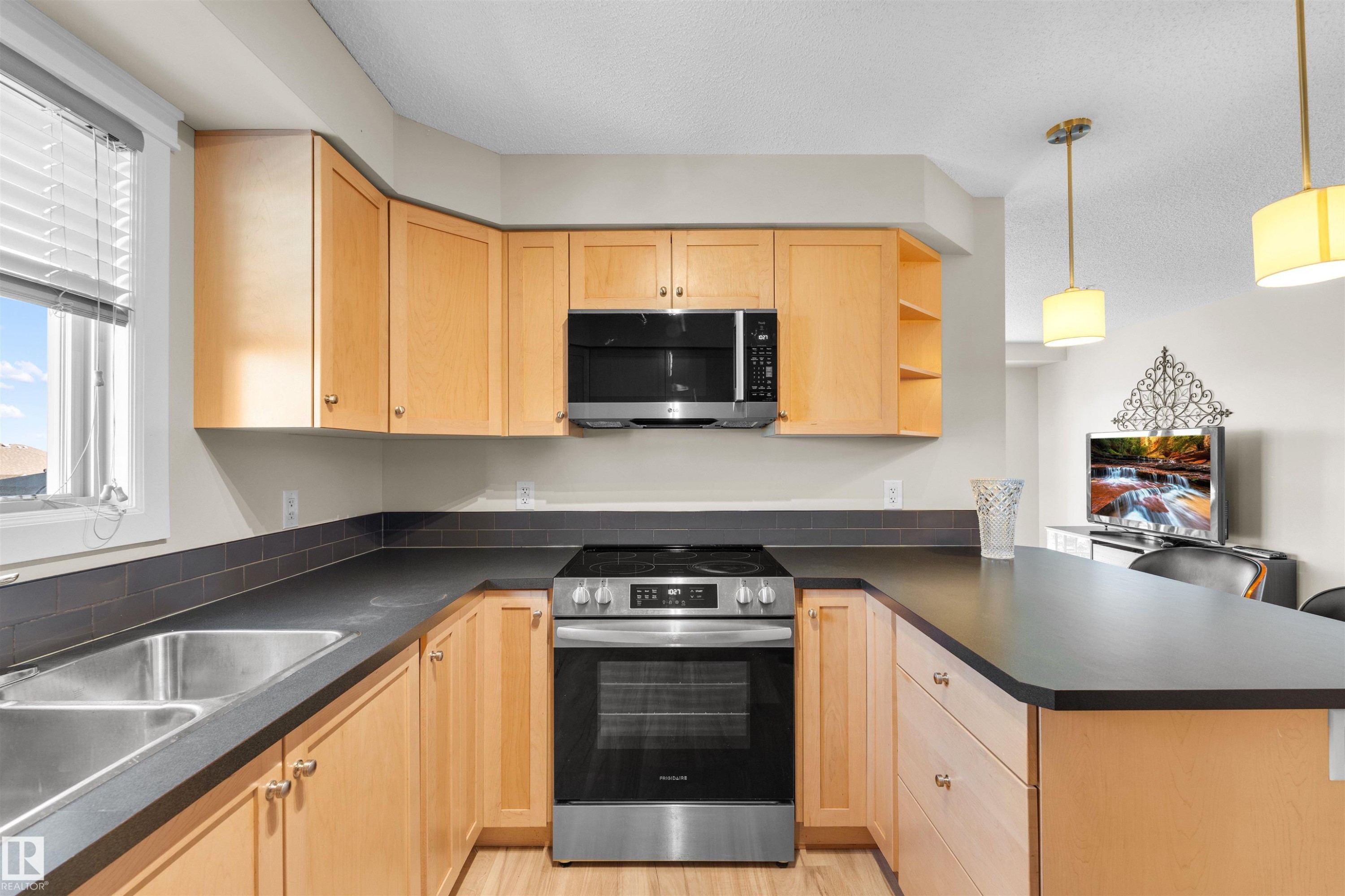 U-shaped kitchen with light wood cabinetry, dark countertops, stainless steel appliances, and a double basin sink - #317 3719 Whitelaw Ln Nw, Edmonton, AB - Indoor Photo Showing Kitchen With Double Sink