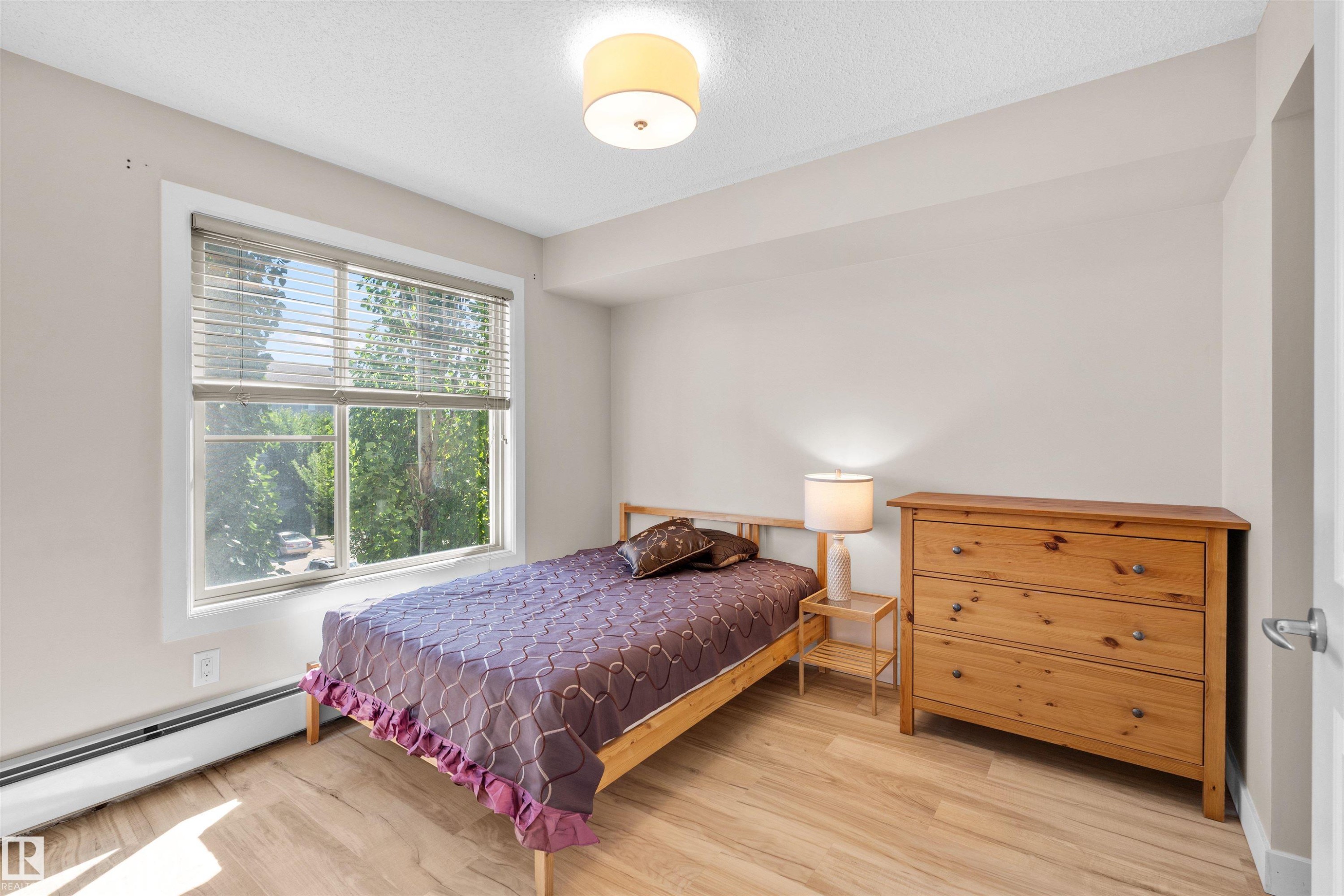 Bright room featuring wood-finish flooring, a large window with blinds, and neutral wall tones - #317 3719 Whitelaw Ln Nw, Edmonton, AB - Indoor Photo Showing Bedroom