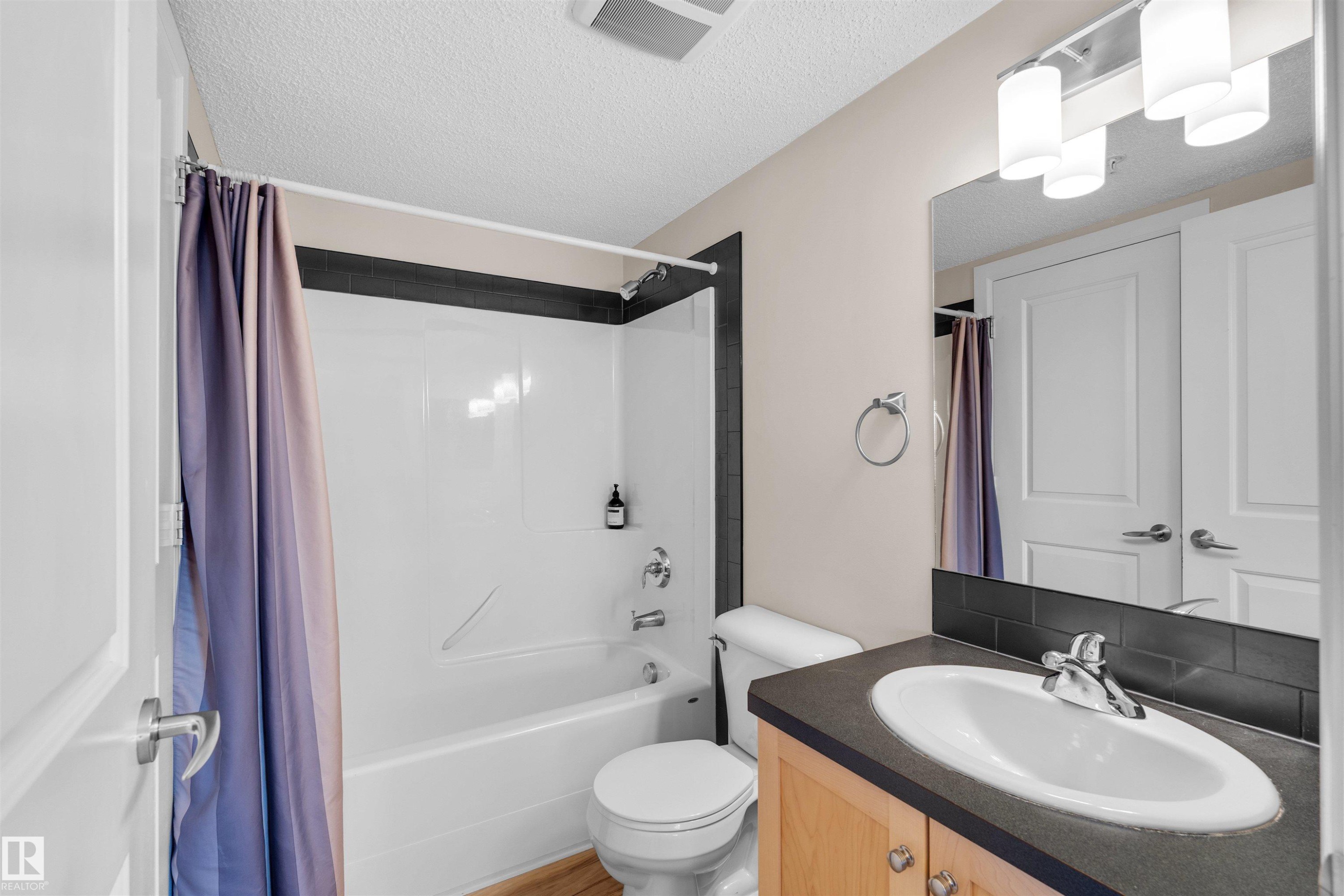 Bathroom featuring a vanity with a light wood-finish cabinet and dark countertop, an oval undermount sink with a chrome faucet, and a large mirror - #317 3719 Whitelaw Ln Nw, Edmonton, AB - Indoor Photo Showing Bathroom