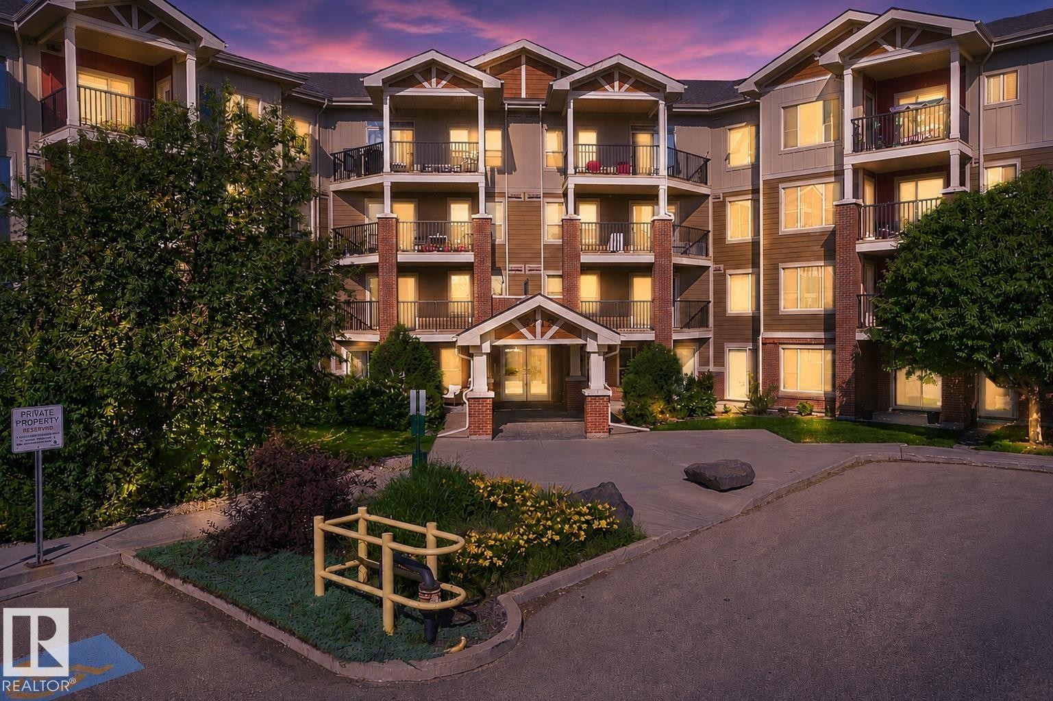 Multi-story building featuring stacked balconies with dark railings, brick column accents, a covered main entrance, and diverse exterior finishes - #317 3719 Whitelaw Ln Nw, Edmonton, AB - Outdoor With Balcony With Facade
