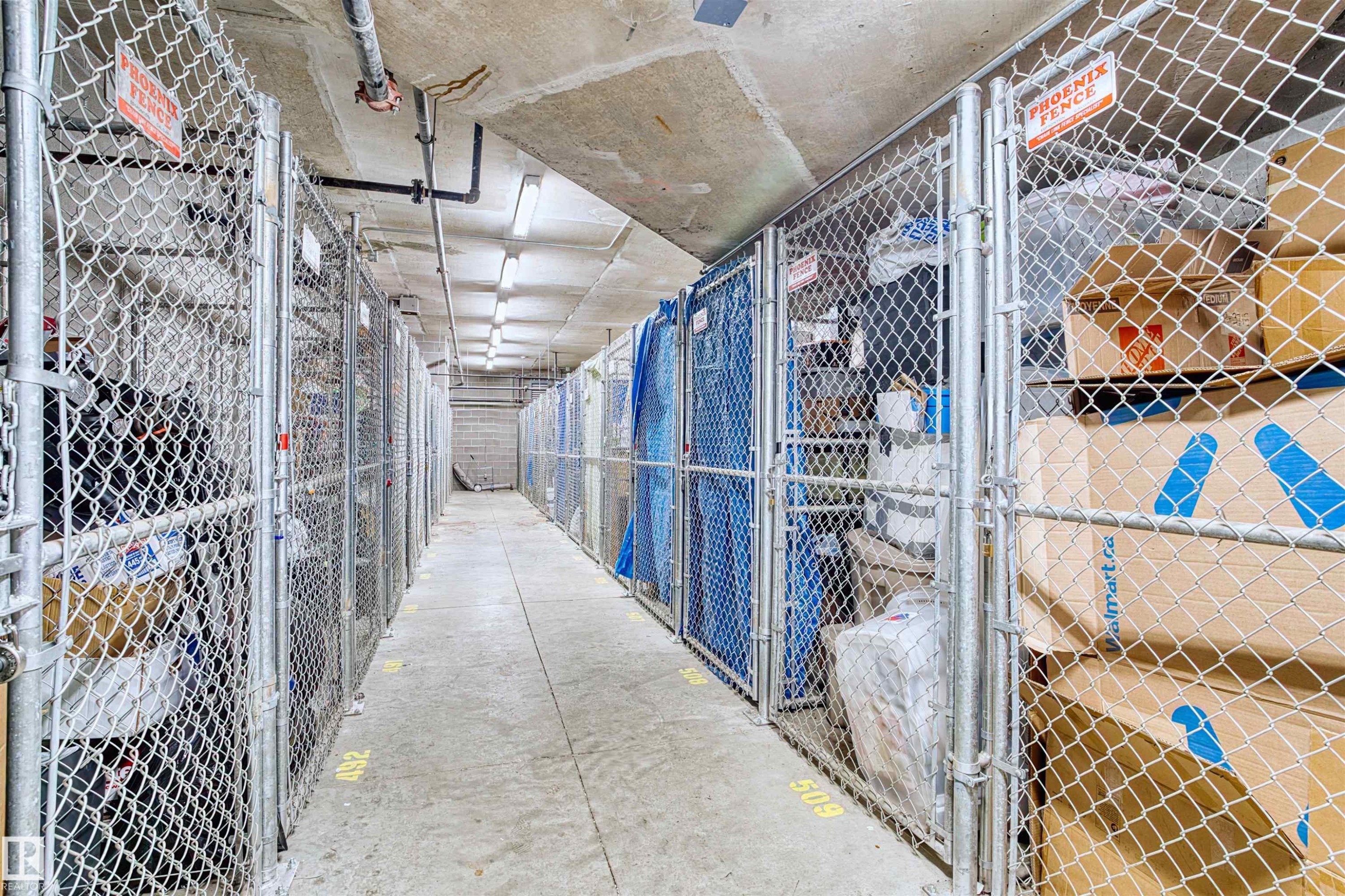 Storage area featuring concrete flooring and ceiling, multiple chain-link storage units, and fluorescent lighting - #317 3719 Whitelaw Ln Nw, Edmonton, AB - Indoor With Storage