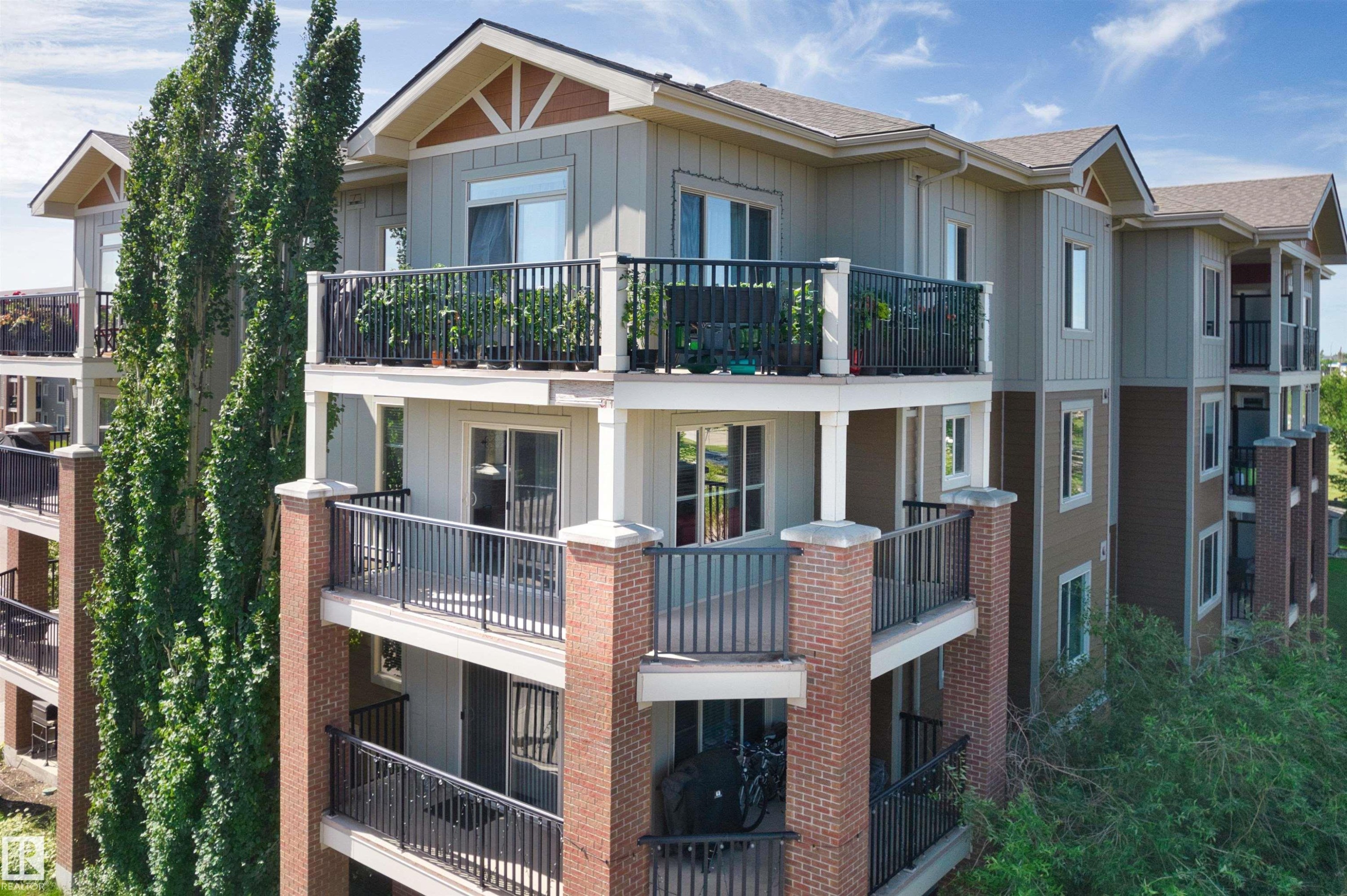 Multi-story building featuring balconies with black railings, brick columns, and a combination of vertical and horizontal siding - #317 3719 Whitelaw Ln Nw, Edmonton, AB - Outdoor With Balcony