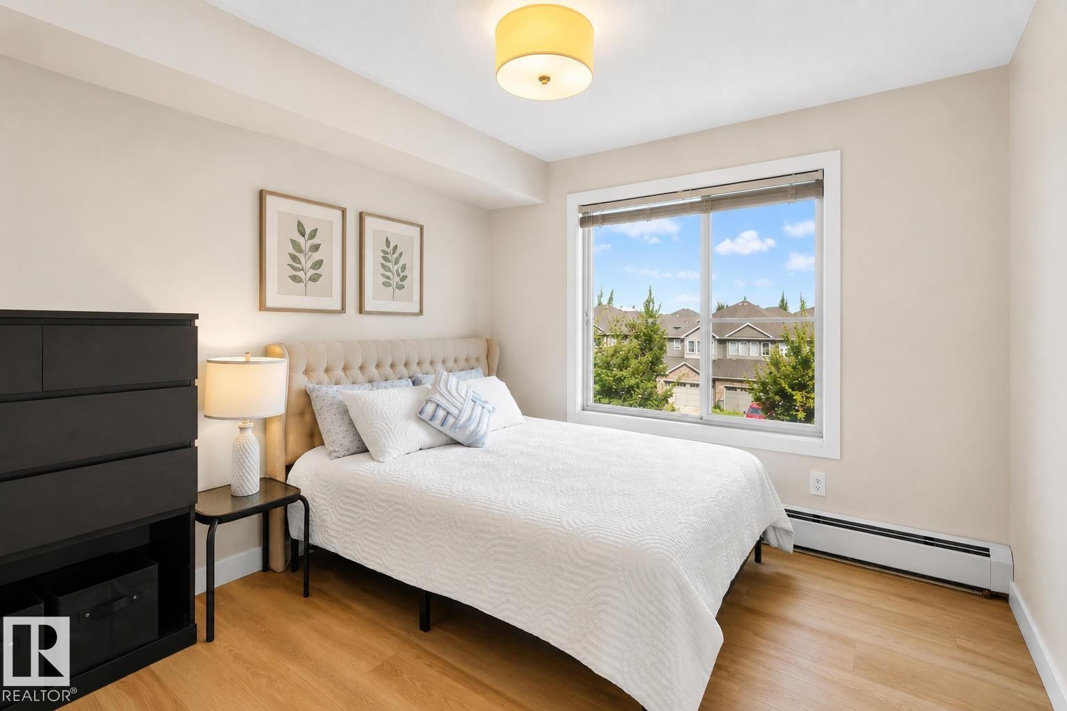 Bedroom featuring a large window, light wood-finish flooring, and a baseboard heating unit - #317 3719 Whitelaw Ln Nw, Edmonton, AB - Indoor Photo Showing Bedroom
