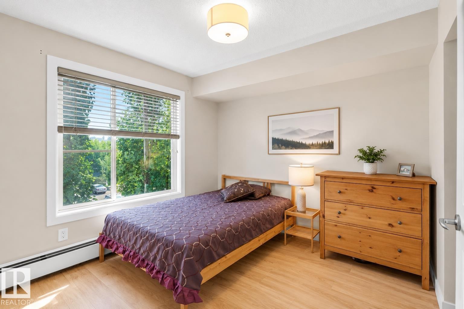 Expansive window providing abundant natural light, wood-finish flooring, overhead drum light fixture, and neutral wall tones - #317 3719 Whitelaw Ln Nw, Edmonton, AB - Indoor Photo Showing Bedroom