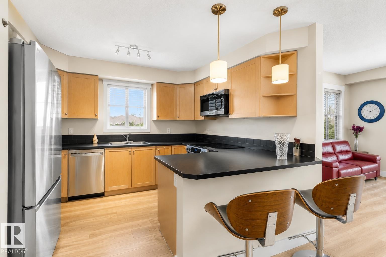 Kitchen featuring light wood cabinetry, dark countertops, stainless steel appliances, and wood-finish flooring - #317 3719 Whitelaw Ln Nw, Edmonton, AB - Indoor Photo Showing Kitchen With Double Sink