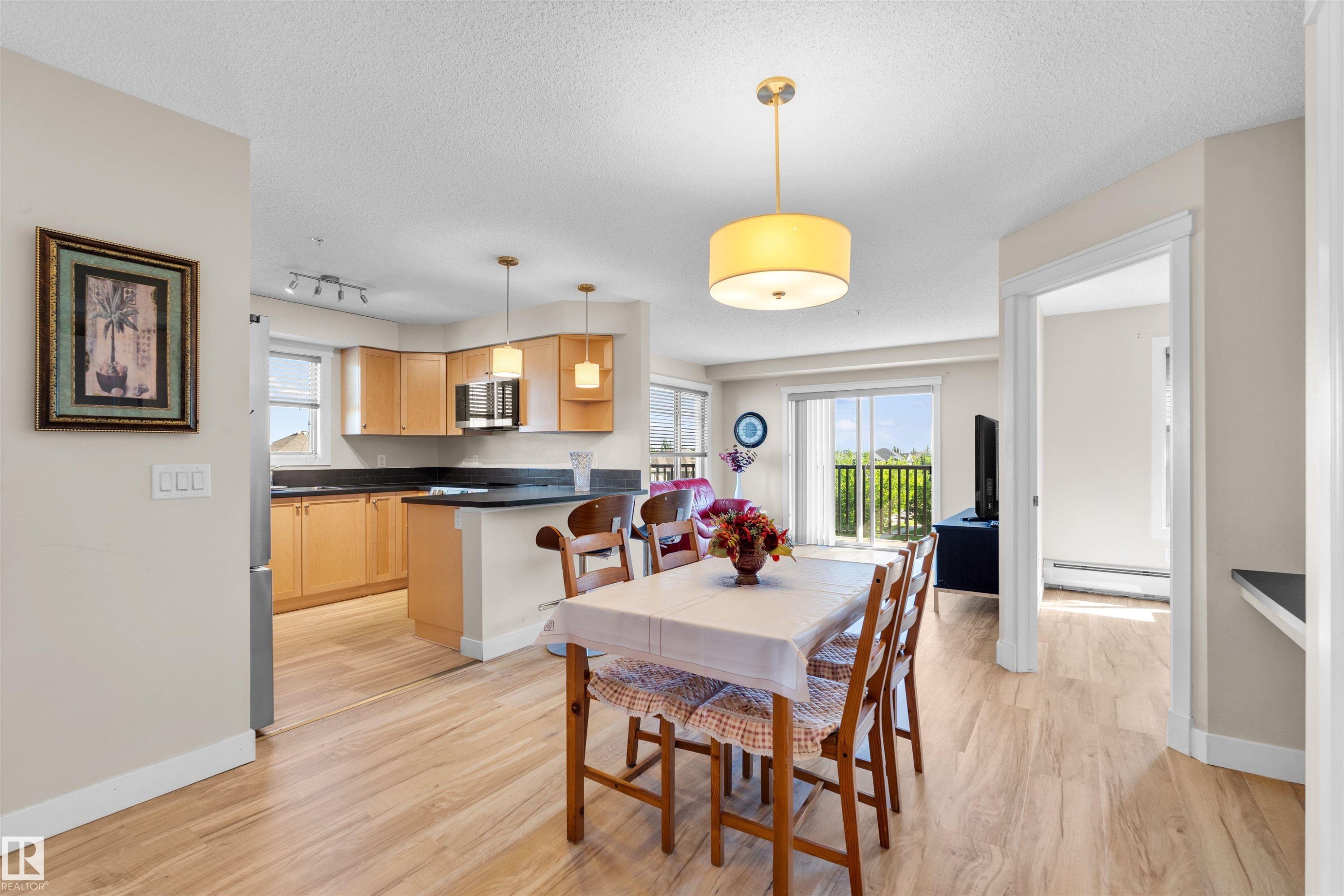Open-concept living space featuring wood-finish flooring, a kitchen with light wood cabinetry and dark countertops, and a dining area - #317 3719 Whitelaw Ln Nw, Edmonton, AB - Indoor Photo Showing Other Room