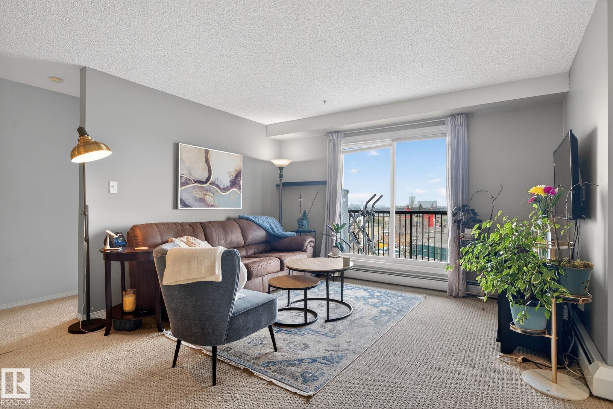 Living area featuring a sliding glass door to a private balcony, neutral wall color, and carpet flooring - 423 2430 Guardian Road, Edmonton, AB - Indoor Photo Showing Living Room
