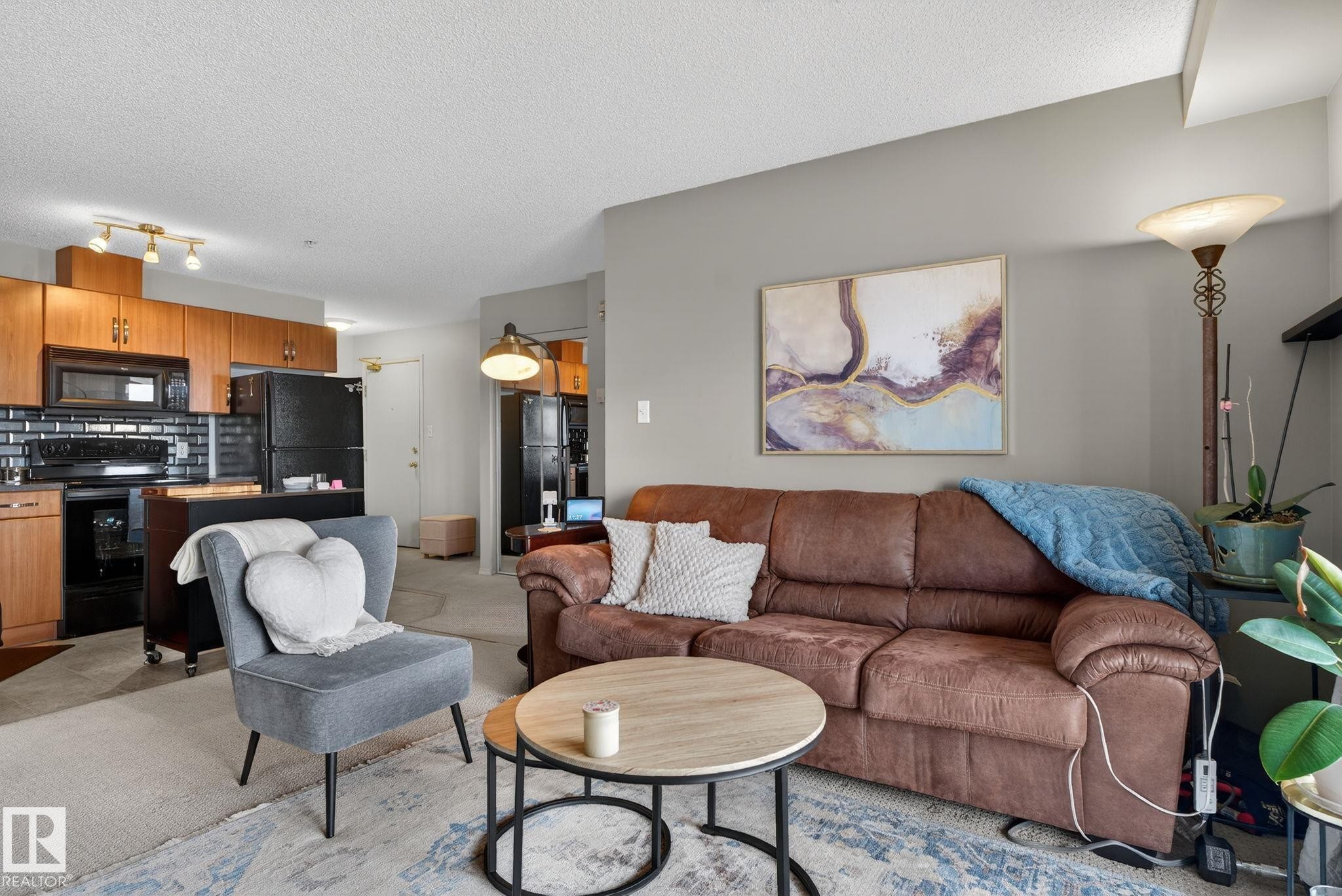 Open-concept living area featuring a kitchen with wood cabinetry, black subway tile backsplash, and black appliances - 423 2430 Guardian Road, Edmonton, AB - Indoor Photo Showing Living Room