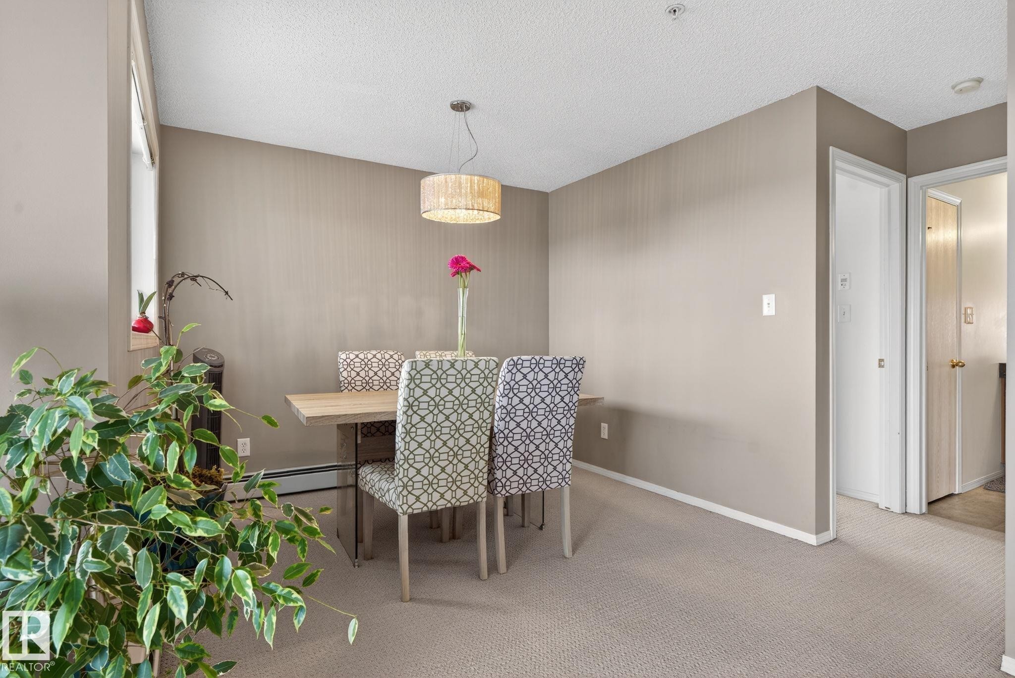 Carpeted dining area featuring neutral-toned walls, a textured ceiling, and a hanging drum-style light fixture - 423 2430 Guardian Road, Edmonton, AB - Indoor Photo Showing Other Room