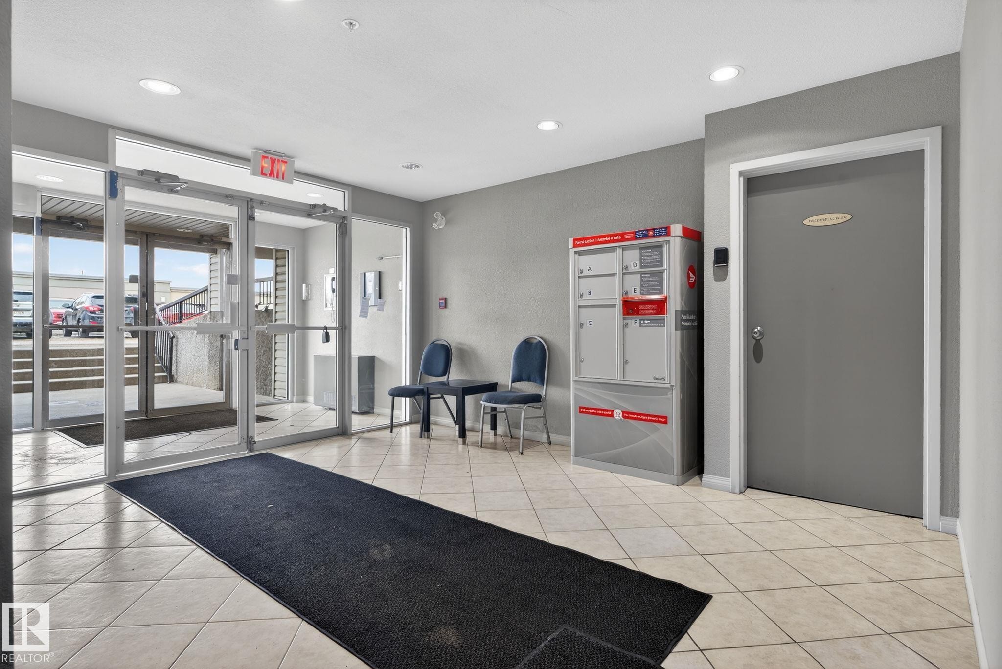 Building entry featuring large glass doors, light-toned tile flooring, recessed ceiling lighting, and a mail delivery system - 423 2430 Guardian Road, Edmonton, AB - Indoor Photo Showing Gym Room