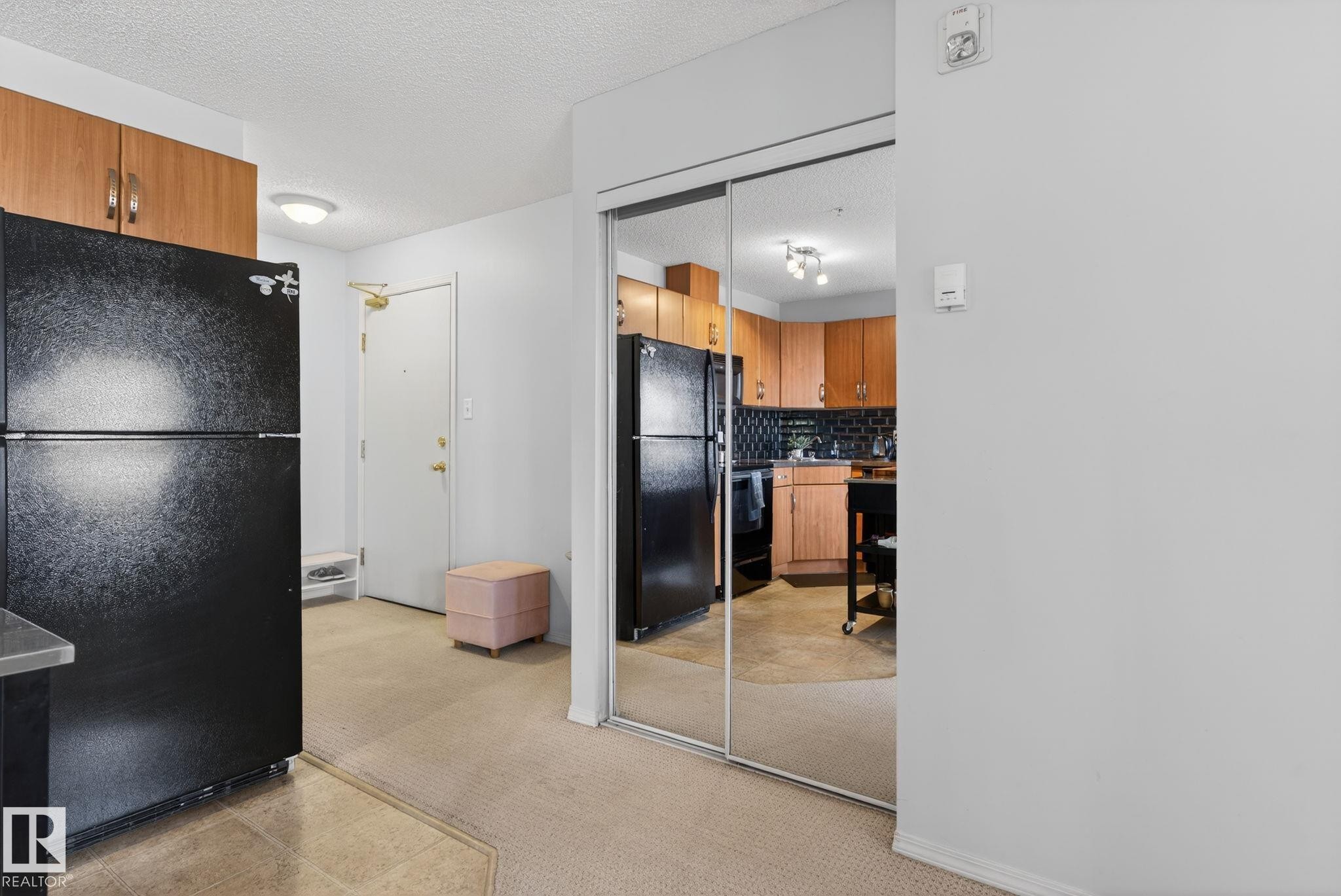 Kitchen area featuring a black refrigerator, wood-finish cabinetry, and a black tile backsplash - 423 2430 Guardian Road, Edmonton, AB - Indoor Photo Showing Kitchen
