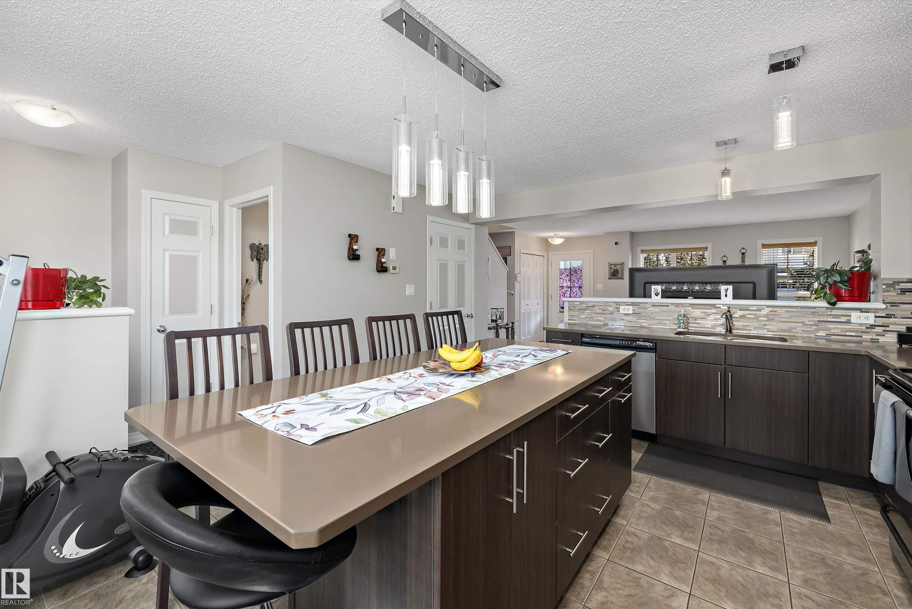 Contemporary kitchen featuring a large island with a solid surface countertop, dark wood-finish cabinetry, stainless steel appliances, a mosaic tile backsplash, and recessed lighting - 4688 Crabapple Run Sw, Edmonton, AB - Indoor Photo Showing Kitchen