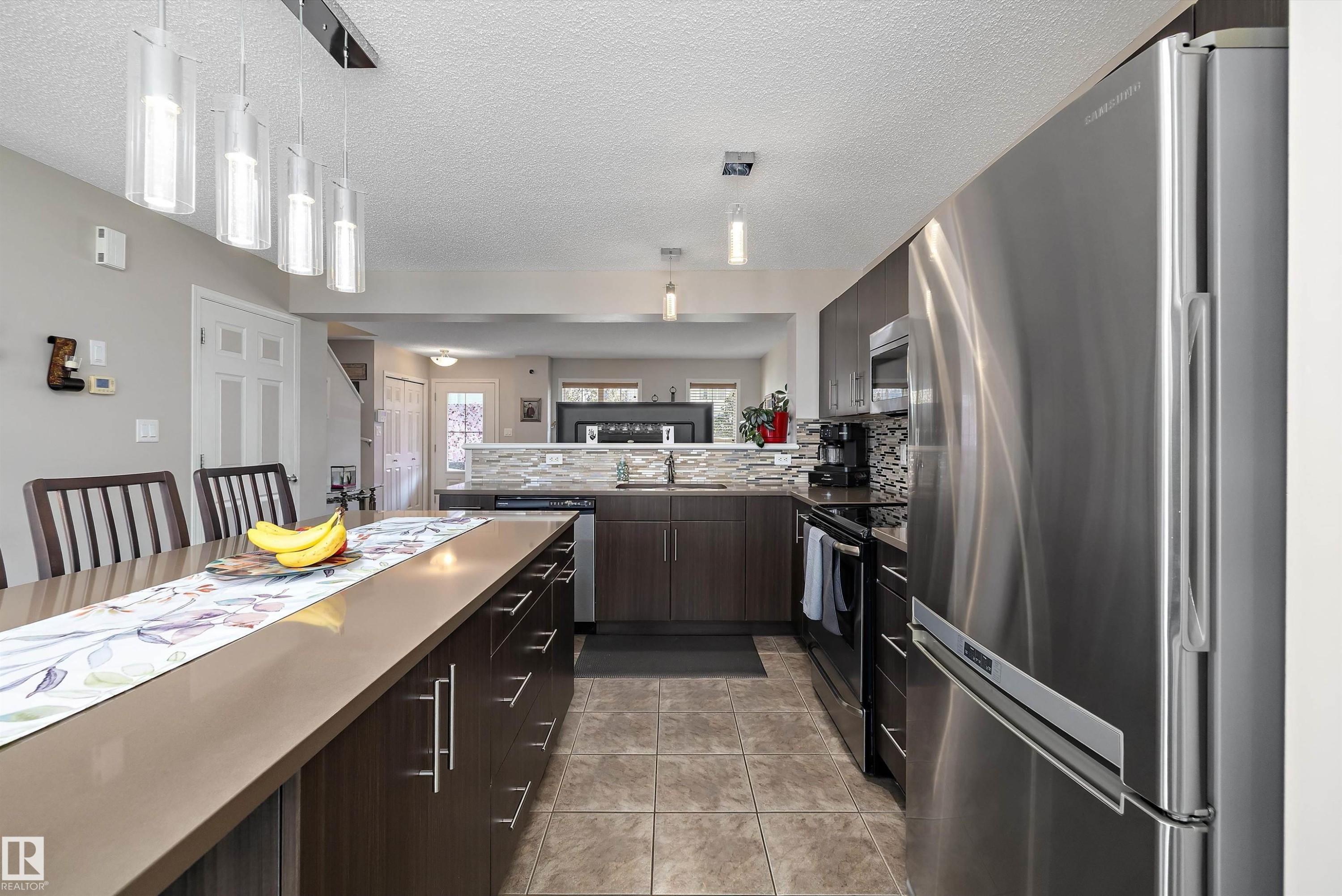 Kitchen featuring an expansive island with seating, dark wood-finish cabinetry, stainless steel appliances, and tile flooring - 4688 Crabapple Run Sw, Edmonton, AB - Indoor Photo Showing Kitchen With Upgraded Kitchen
