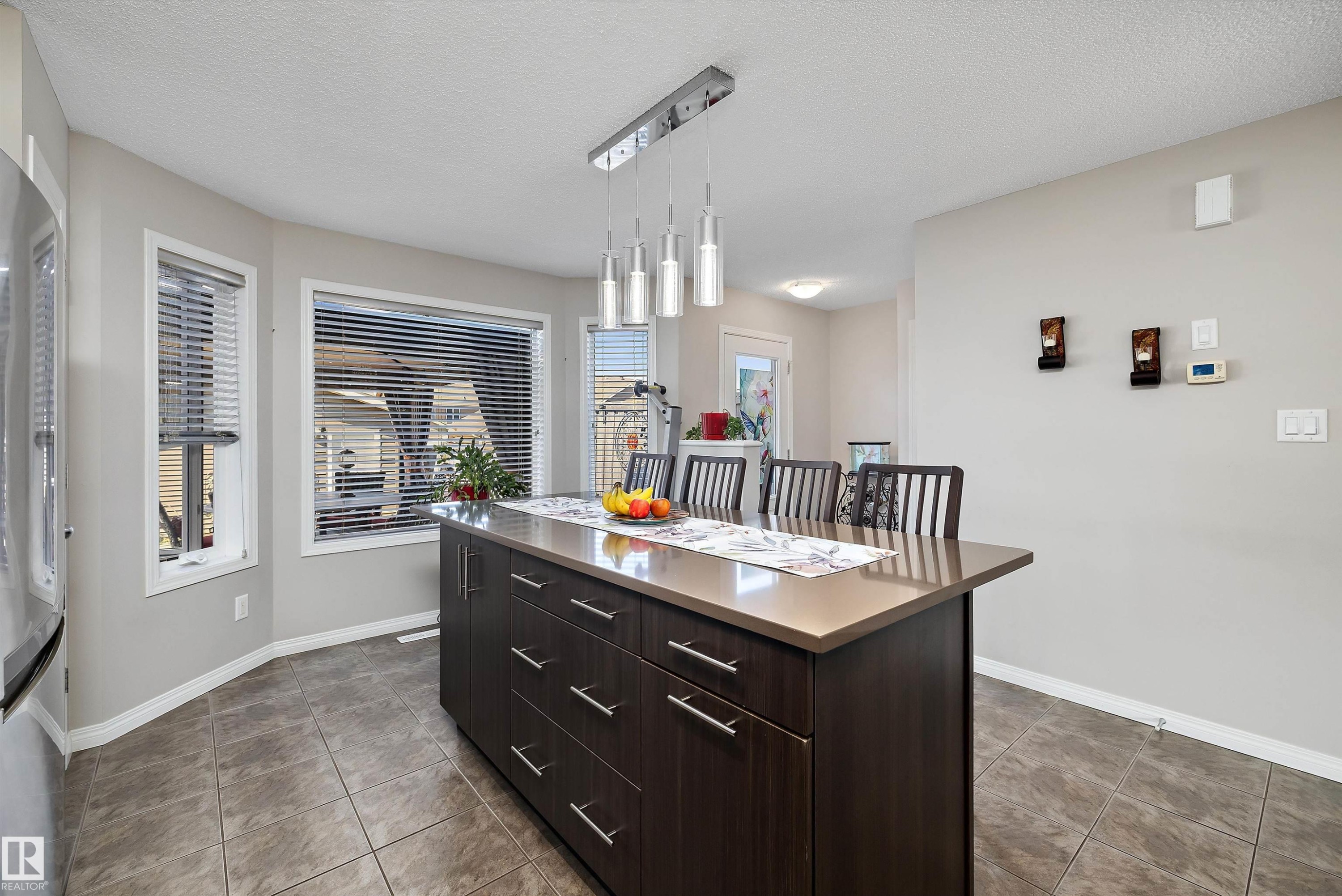 Kitchen island featuring a stone-finish countertop, dark wood-finish cabinetry, and contemporary pendant lighting - 4688 Crabapple Run Sw, Edmonton, AB - Indoor