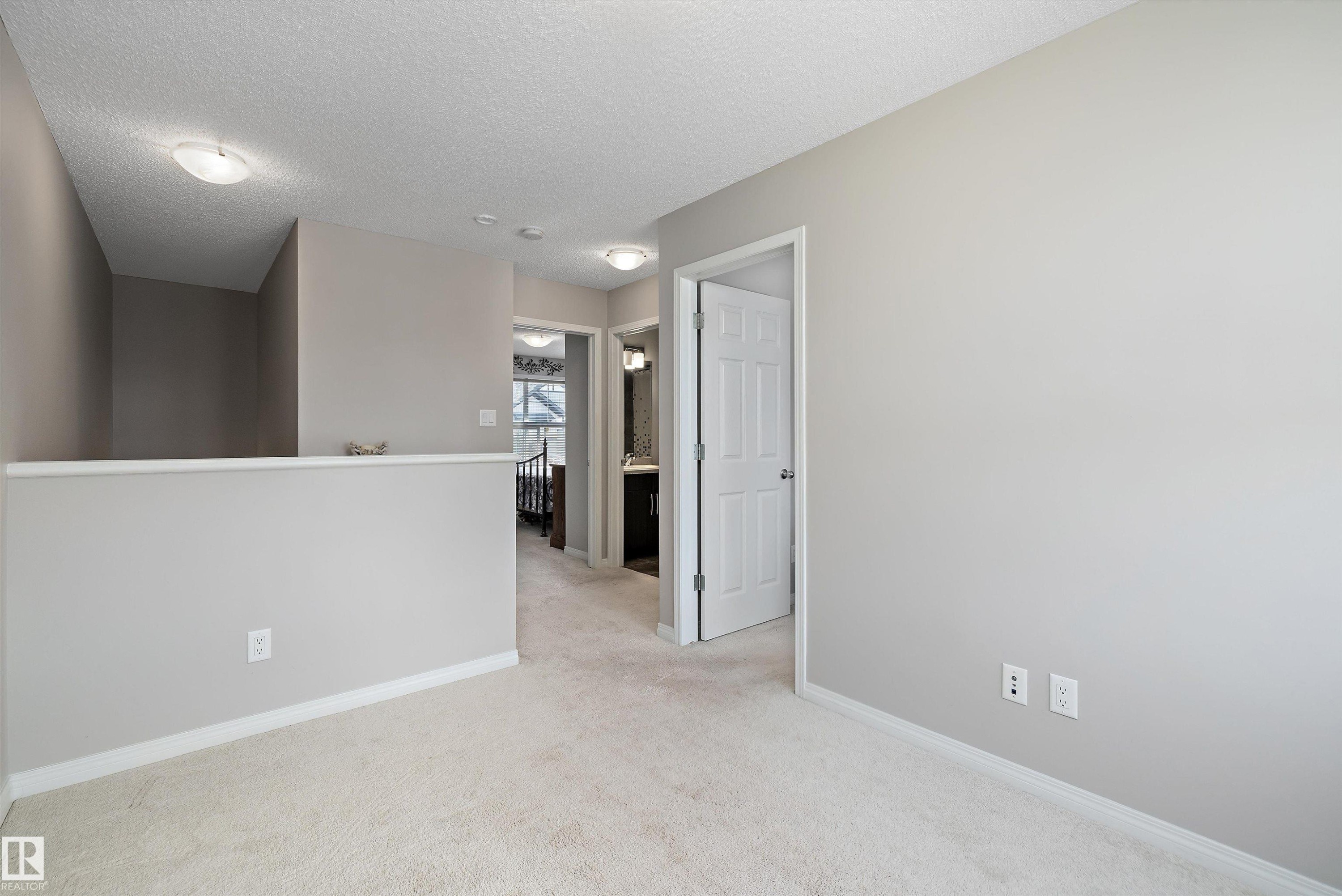 Carpeted upper-level hall featuring a half-wall railing, overhead flush mount lighting, and neutral wall tones - 4688 Crabapple Run Sw, Edmonton, AB - Indoor Photo Showing Other Room