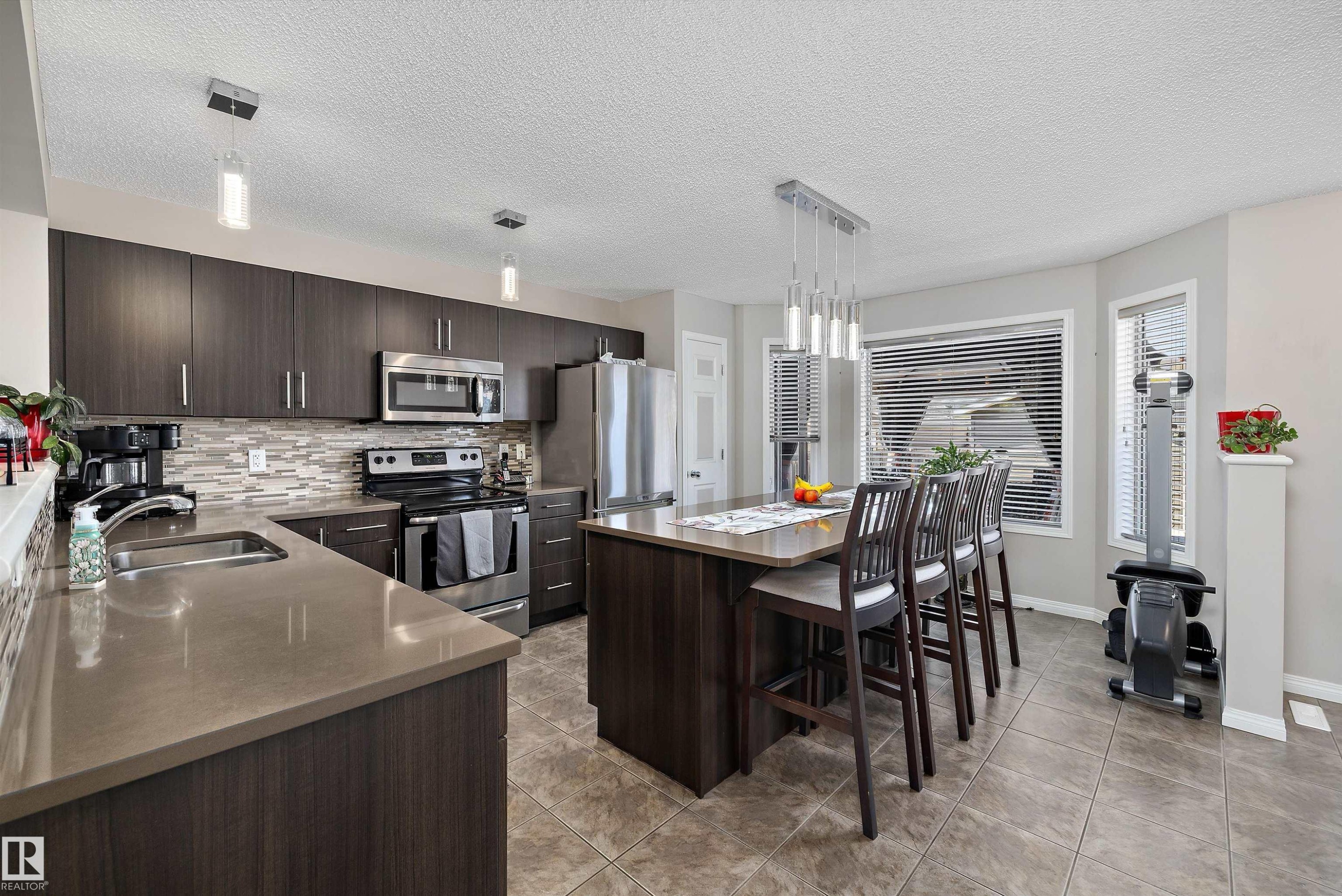 Kitchen featuring dark cabinetry, stainless steel appliances, a multi-toned tile backsplash, and an island with seating - 4688 Crabapple Run Sw, Edmonton, AB - Indoor Photo Showing Kitchen With Double Sink With Upgraded Kitchen