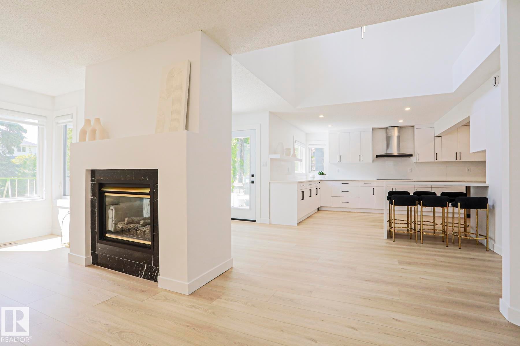Open-concept living space featuring light wood-finish flooring, a contemporary fireplace with a dark stone surround, and an expansive kitchen - 11347 10 Avenue, Edmonton, AB - Indoor With Fireplace