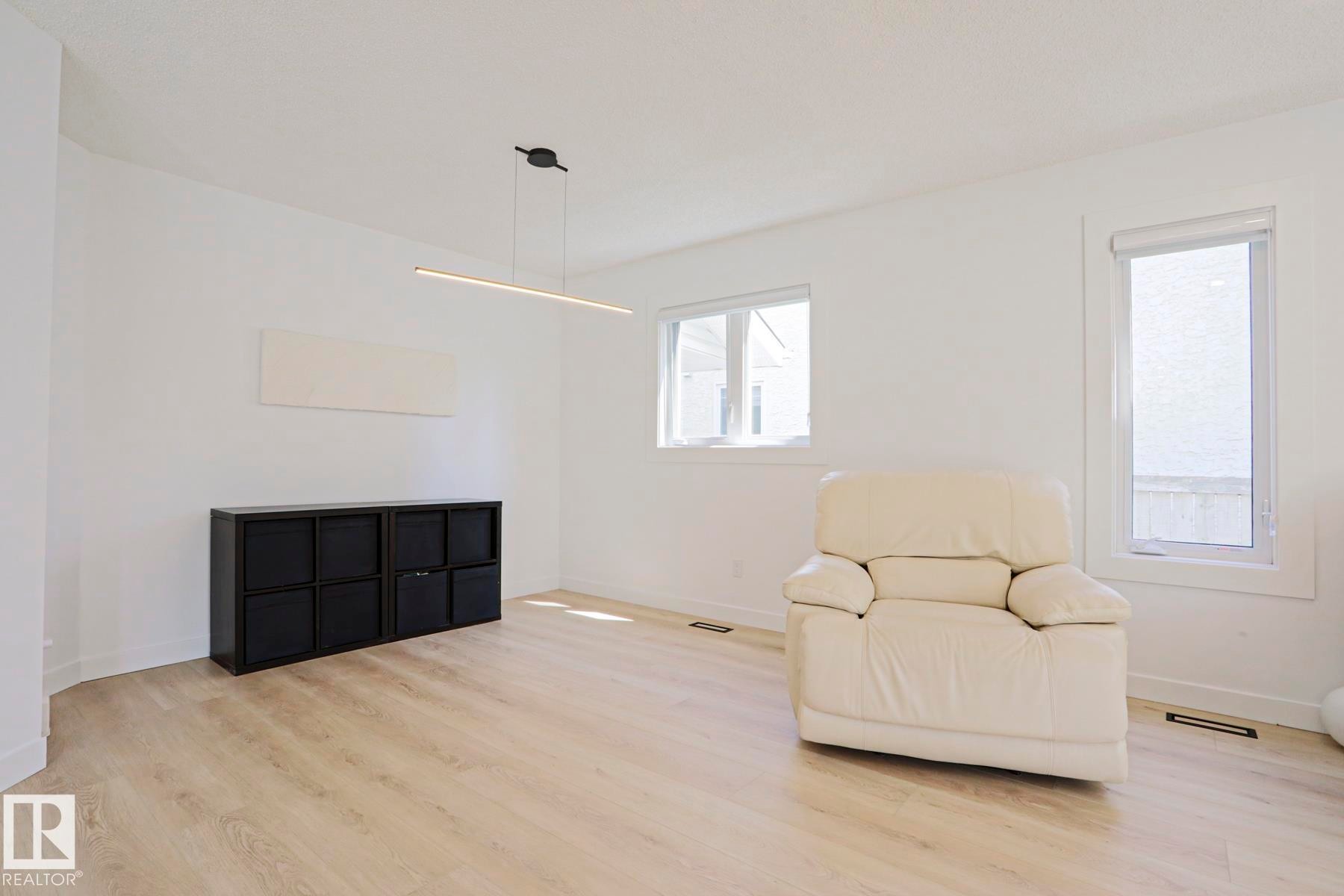 Spacious room featuring light wood-finish flooring, white painted walls, and multiple windows - 11347 10 Avenue, Edmonton, AB - Indoor Photo Showing Living Room