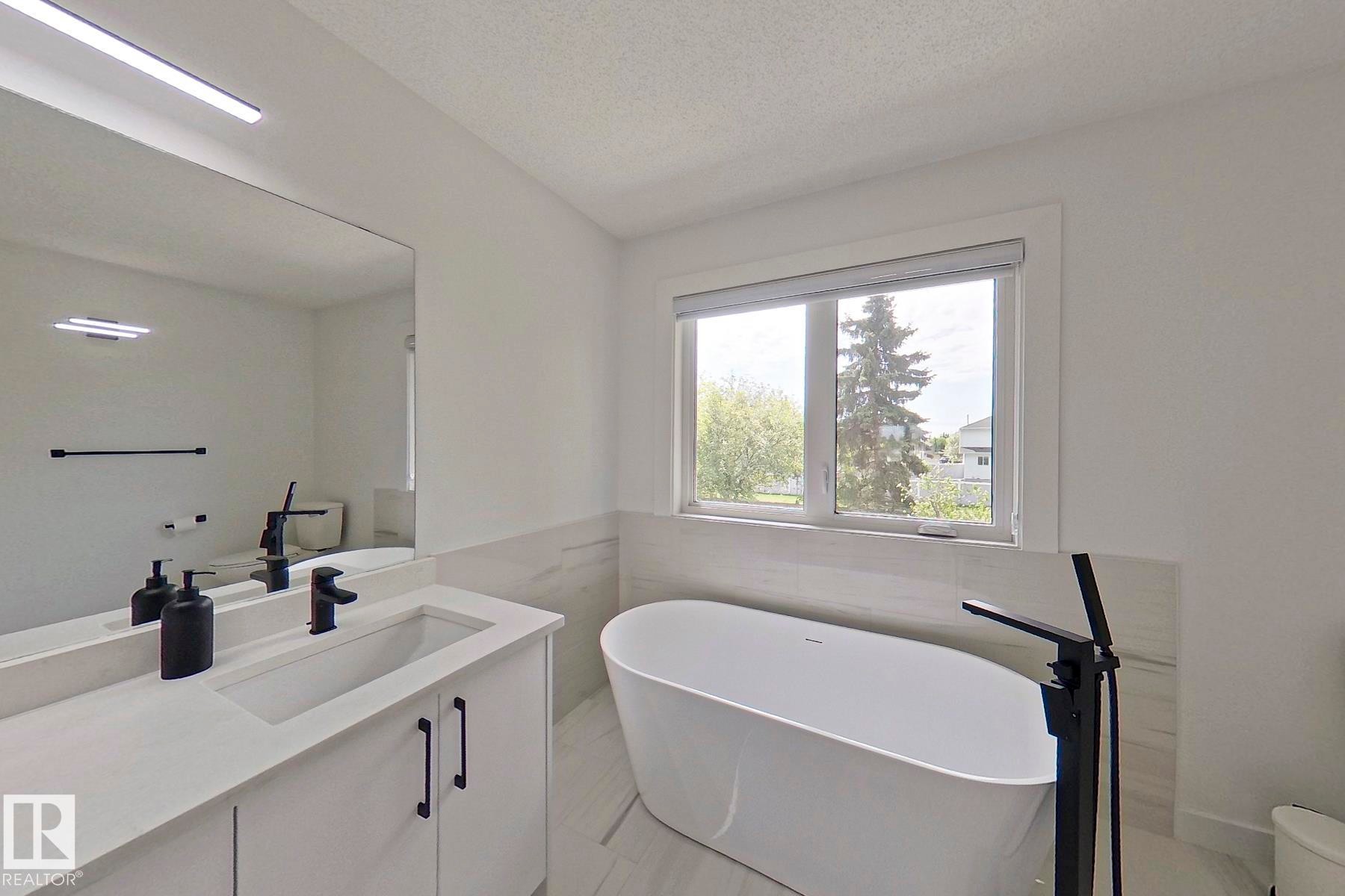 Freestanding soaking tub with a floor-mounted matte black faucet - 11347 10 Avenue, Edmonton, AB - Indoor