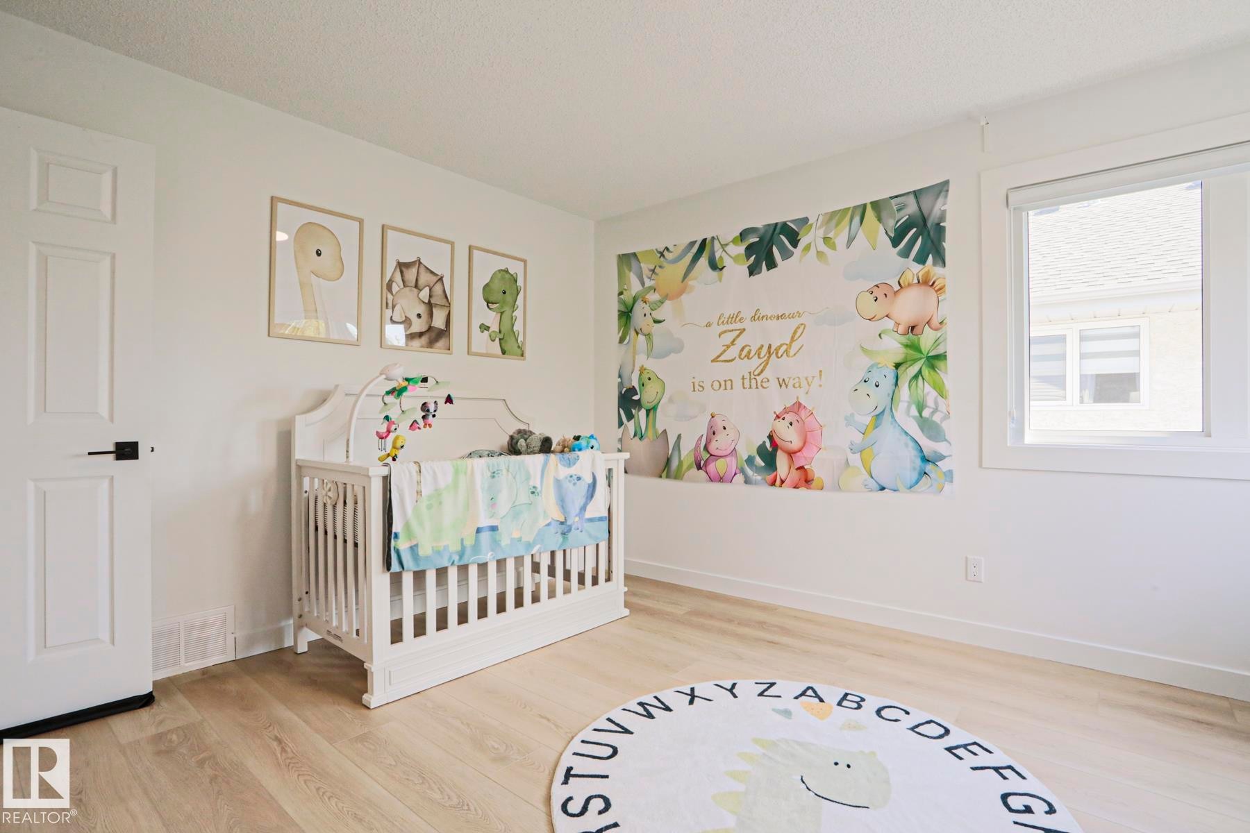 Bright room featuring light wood-finish flooring, white painted walls, a white paneled door with black hardware, and a large window - 11347 10 Avenue, Edmonton, AB - Indoor