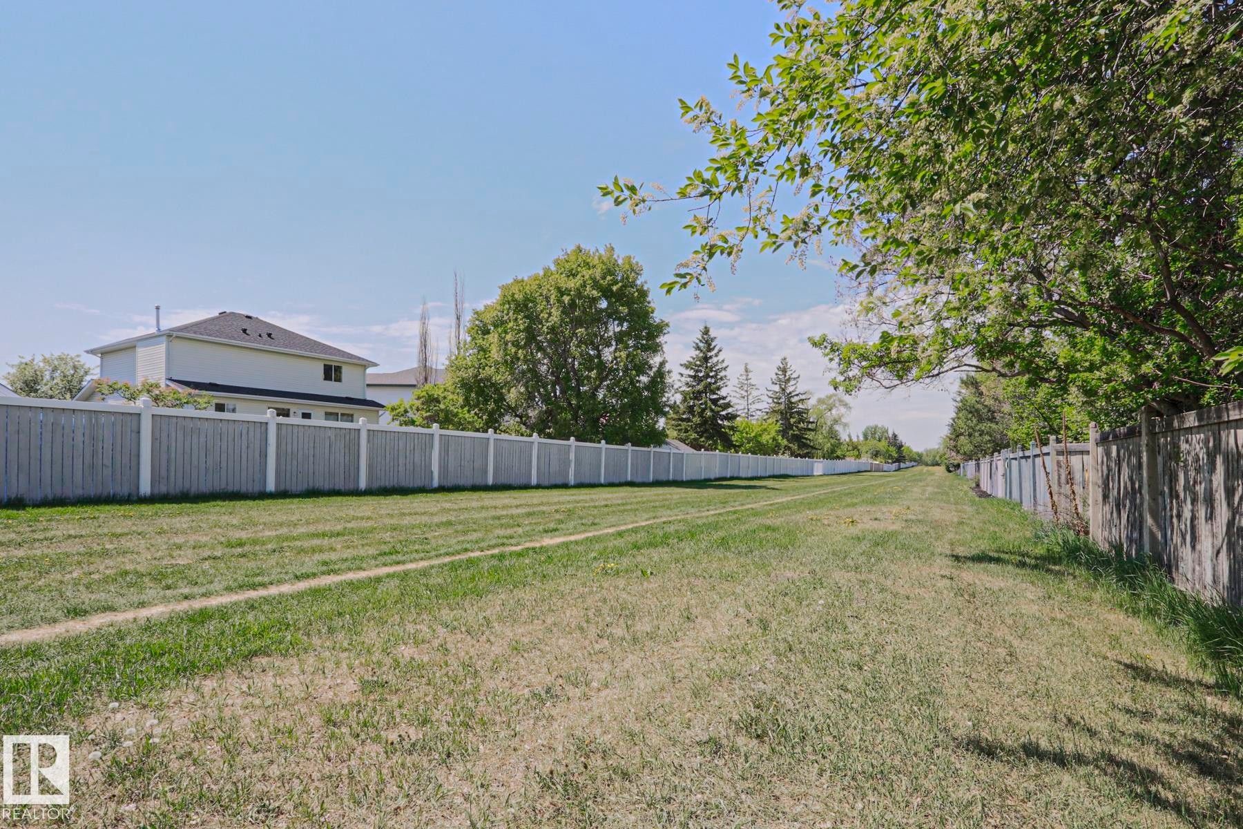 Expansive green space featuring a long stretch of manicured lawn, a light-colored wooden fence, and mature trees providing natural shading - 11347 10 Avenue, Edmonton, AB - Outdoor