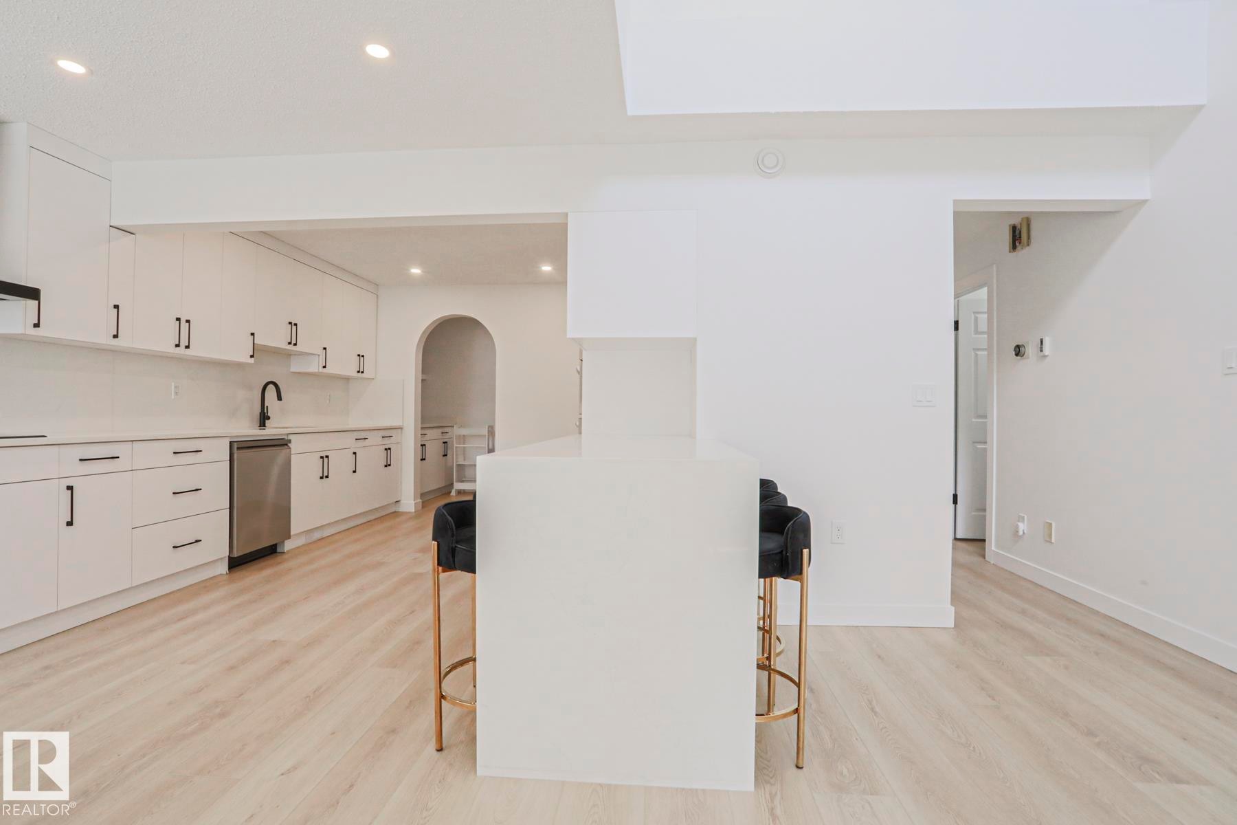 Modern kitchen featuring white cabinetry, stainless steel dishwasher, black faucet, and light wood-finish flooring - 11347 10 Avenue, Edmonton, AB - Indoor Photo Showing Kitchen