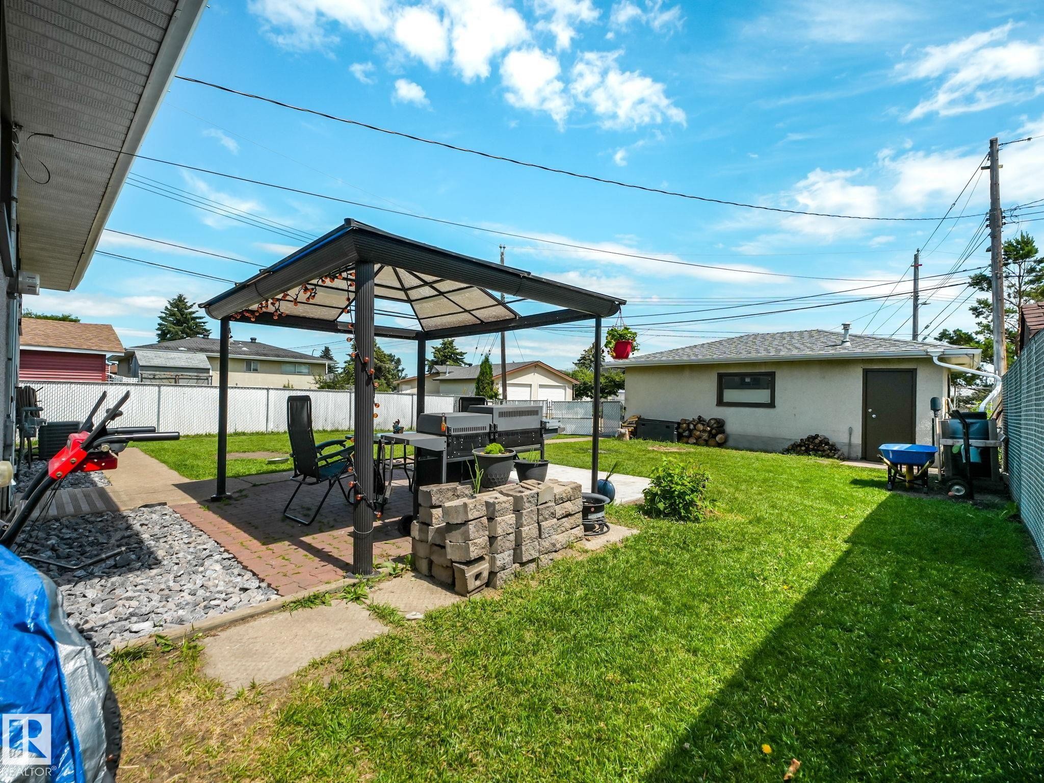 Spacious backyard featuring a covered patio structure, expansive green lawn, and a detached auxiliary building - 13323 58 Street Nw, Edmonton, AB - Outdoor