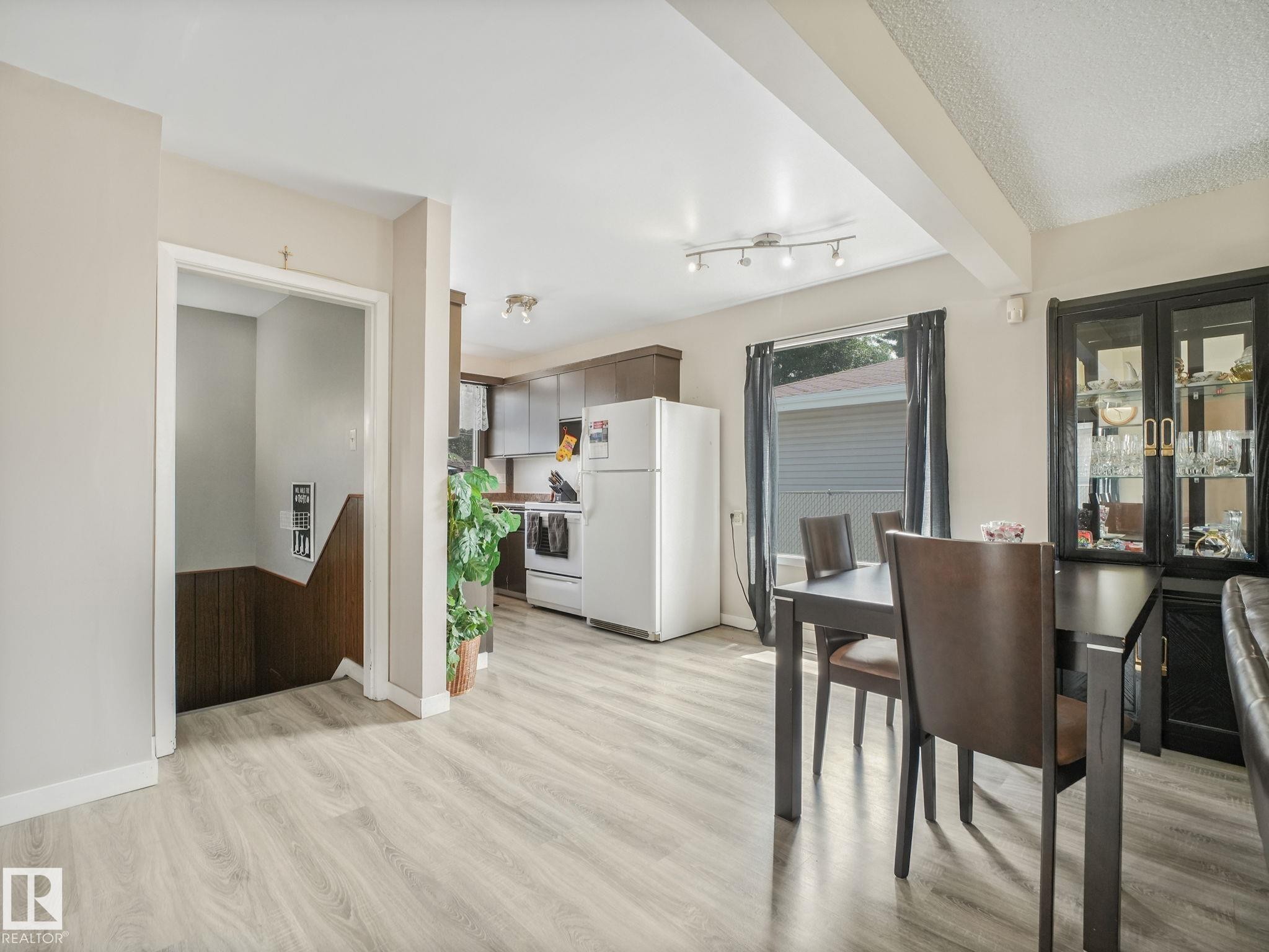 Open-concept living space featuring wood-finish flooring, a kitchen with dark cabinetry and white appliances, and a dining area with track lighting - 13323 58 Street Nw, Edmonton, AB - Indoor