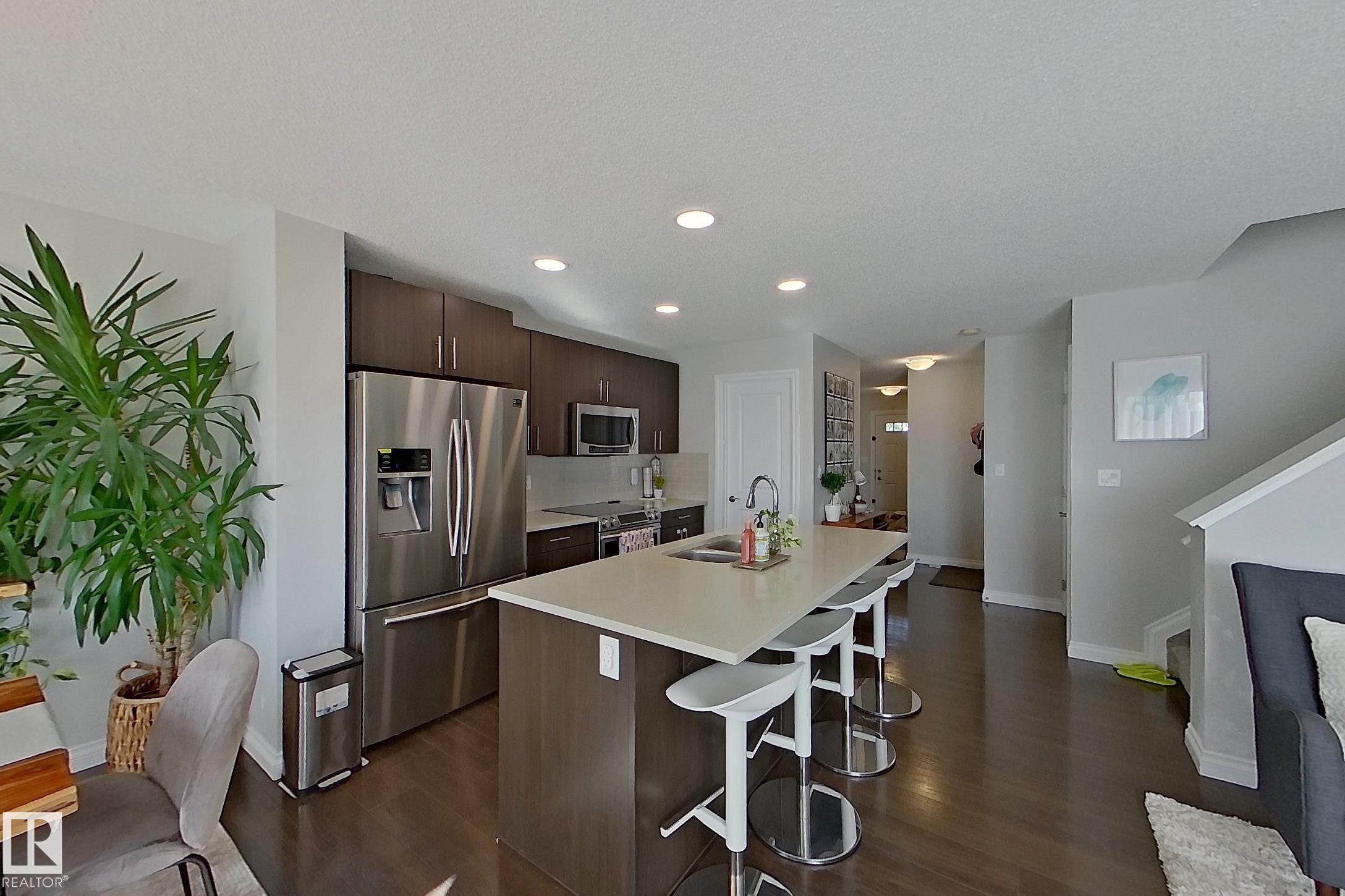 Kitchen featuring a large island with seating, stainless steel appliances, dark wood-finish cabinetry, and recessed lighting - 491 Ebbers Way, Edmonton, AB
