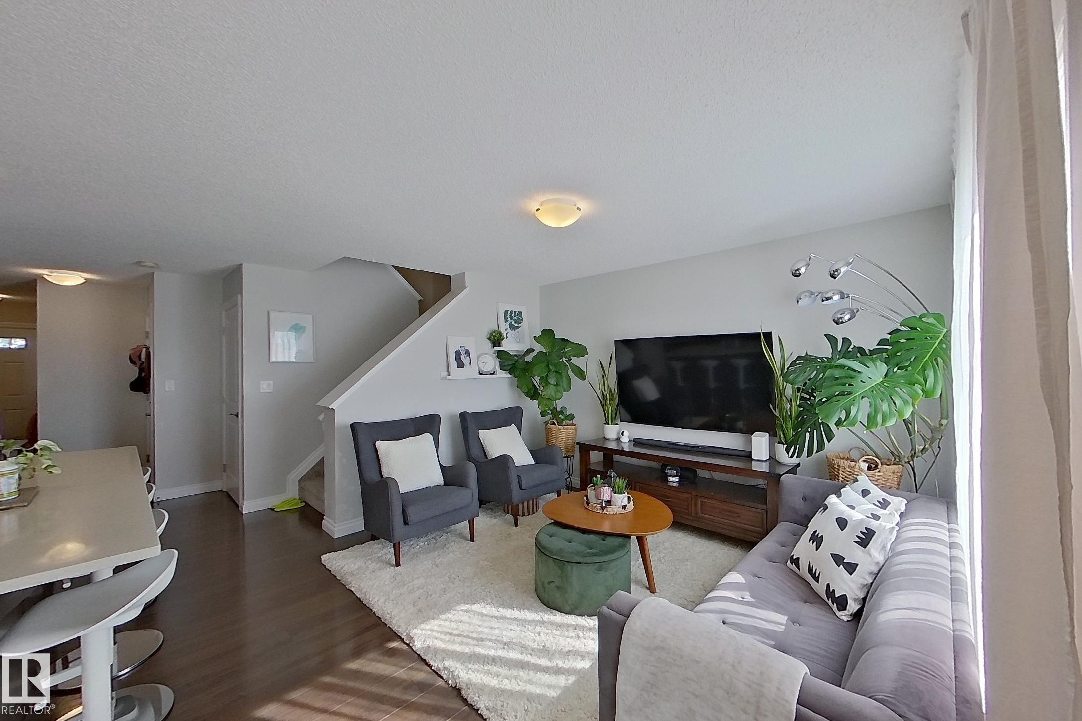 Open-concept living space featuring wood-finish flooring, a contemporary staircase, and light wall finishes - 491 Ebbers Way, Edmonton, AB