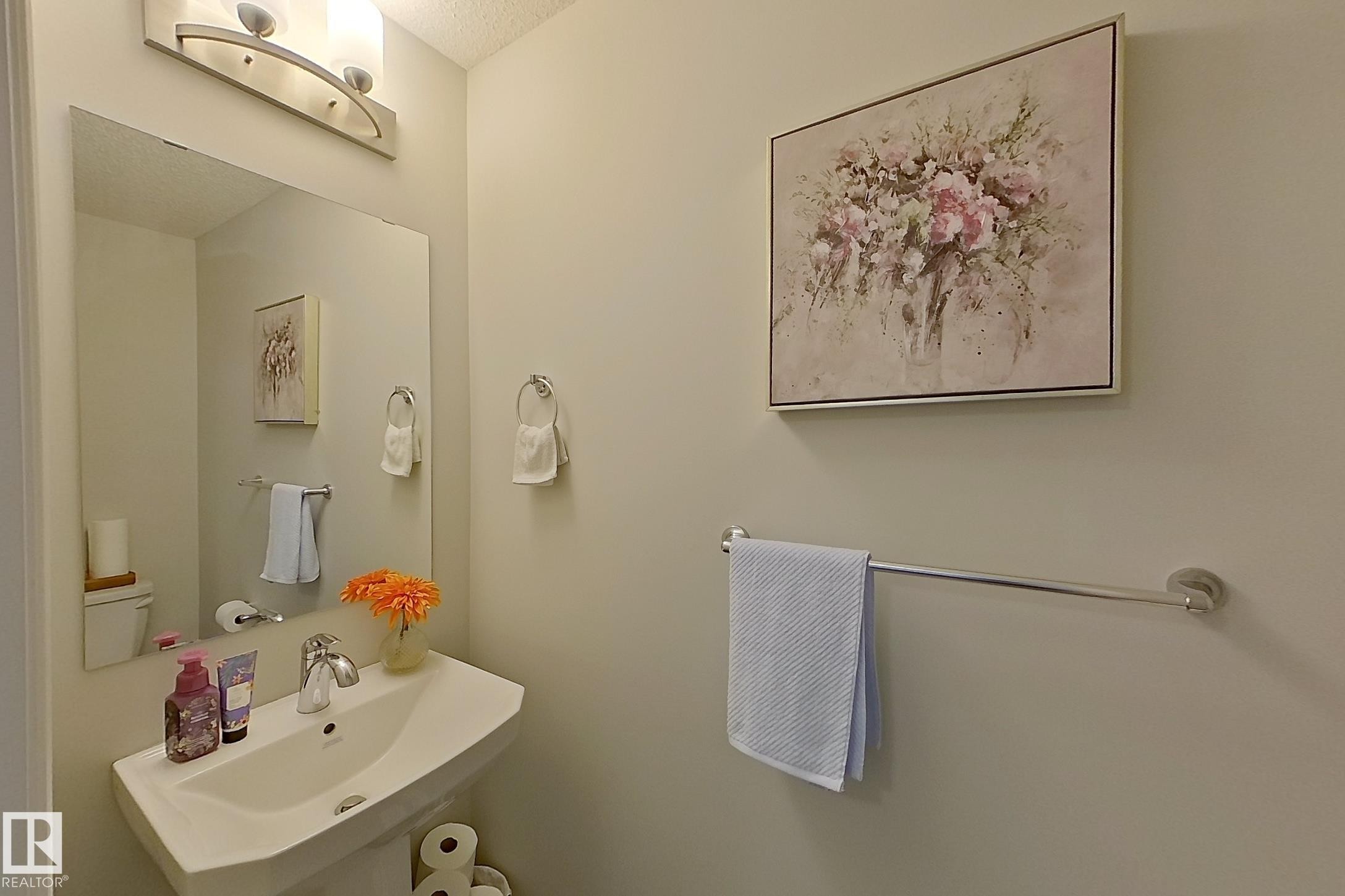 Pedestal sink with chrome faucet, large wall-mounted mirror, and brushed nickel light fixture - 491 Ebbers Way, Edmonton, AB