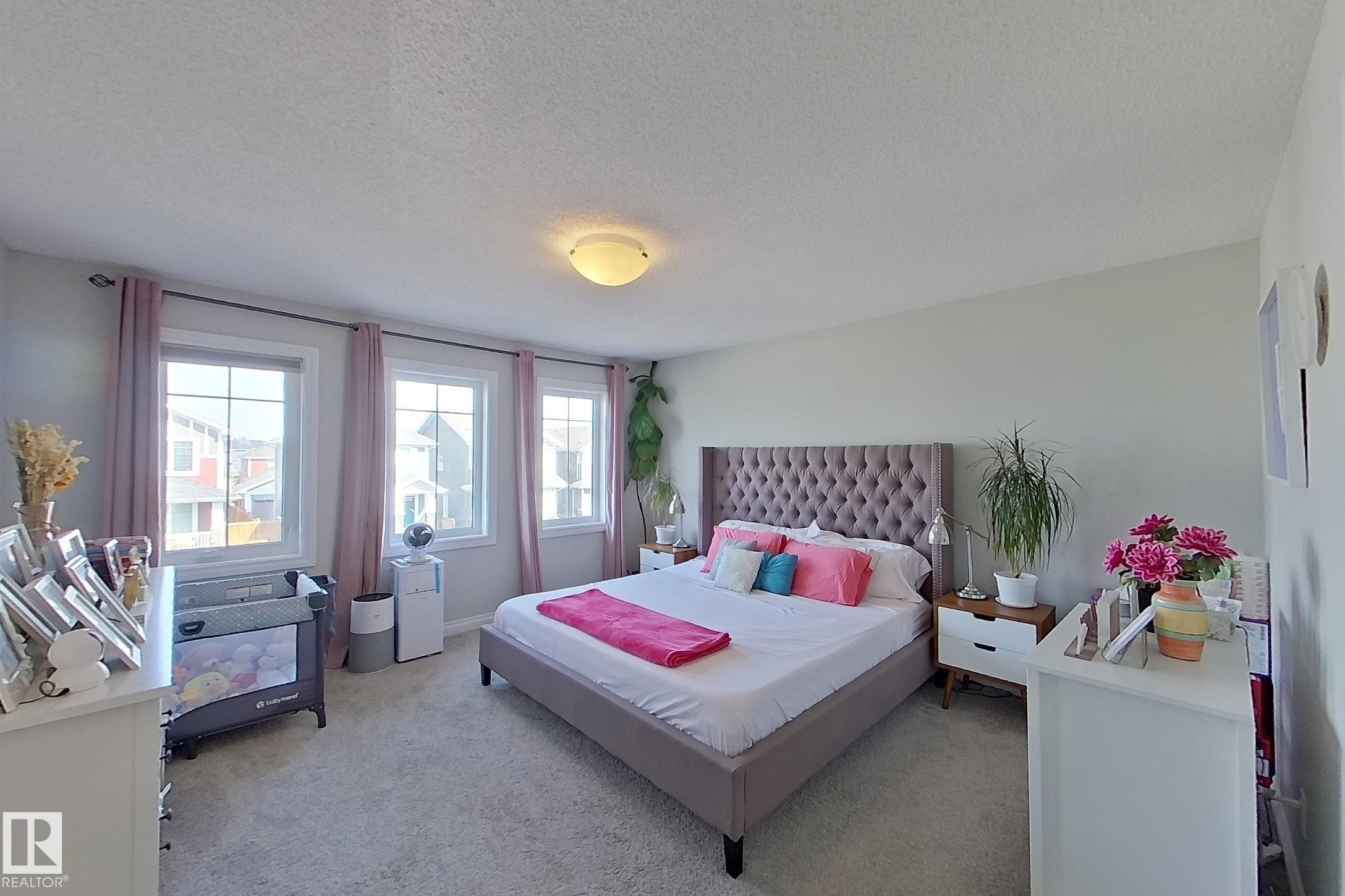Light-filled room featuring three windows with white frames, neutral wall color, and wall-to-wall carpeting - 491 Ebbers Way, Edmonton, AB