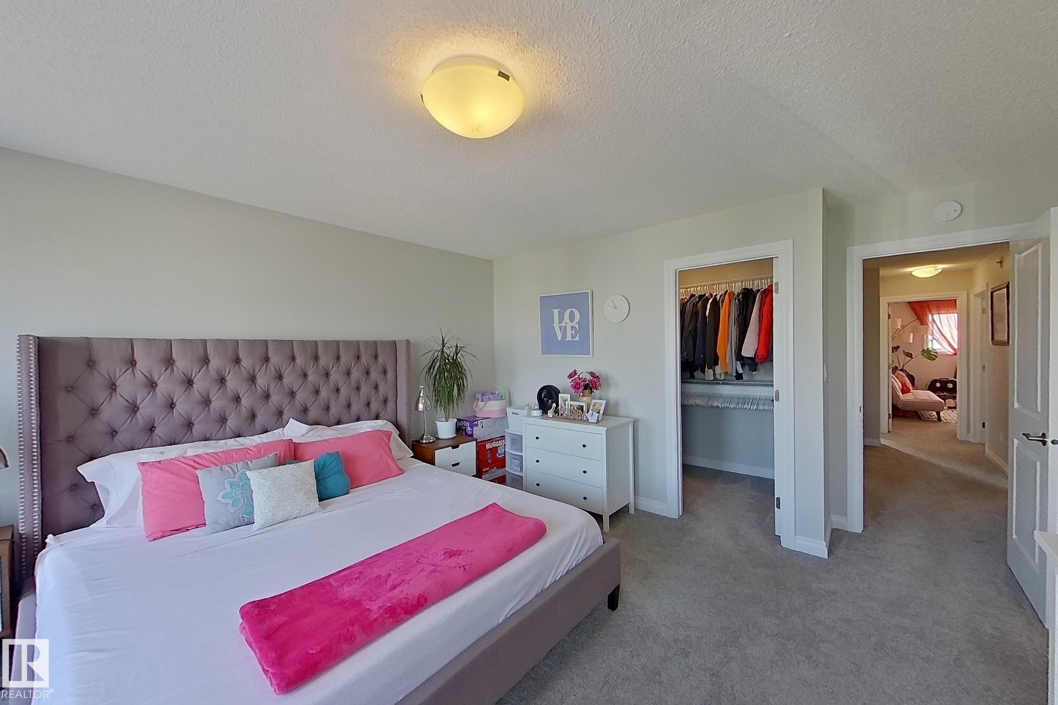 Spacious bedroom featuring light neutral wall paint, carpet flooring, a walk-in closet, and a ceiling-mounted light fixture - 491 Ebbers Way, Edmonton, AB