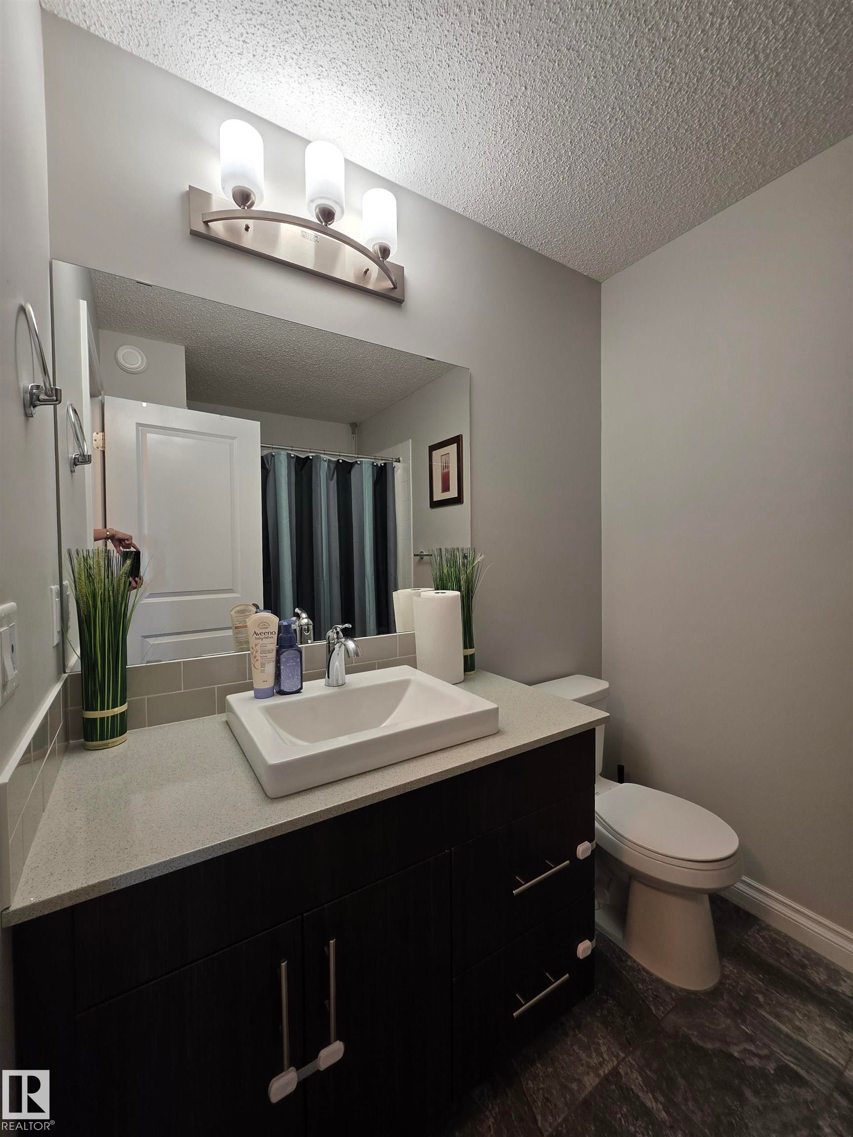 Bathroom featuring a dark wood-finish vanity with an undermount vessel sink, light countertop, and subway tile backsplash - 491 Ebbers Way, Edmonton, AB