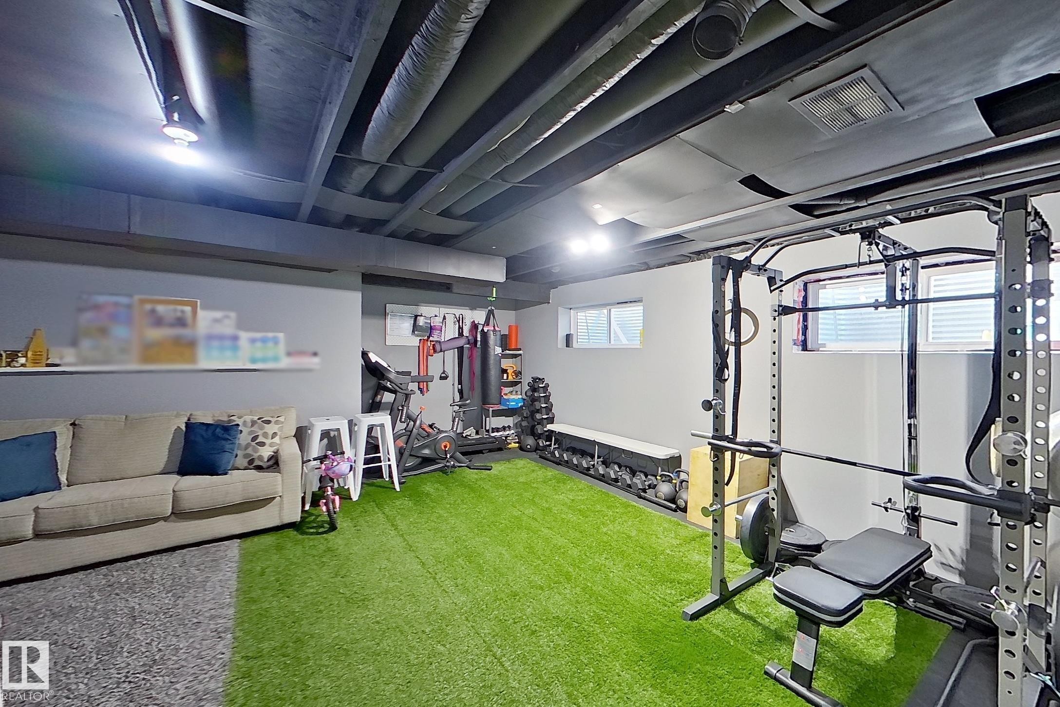 Versatile lower-level space featuring a turf-style flooring, painted exposed ceiling joists, recessed lighting, and wall-mounted shelving - 491 Ebbers Way, Edmonton, AB